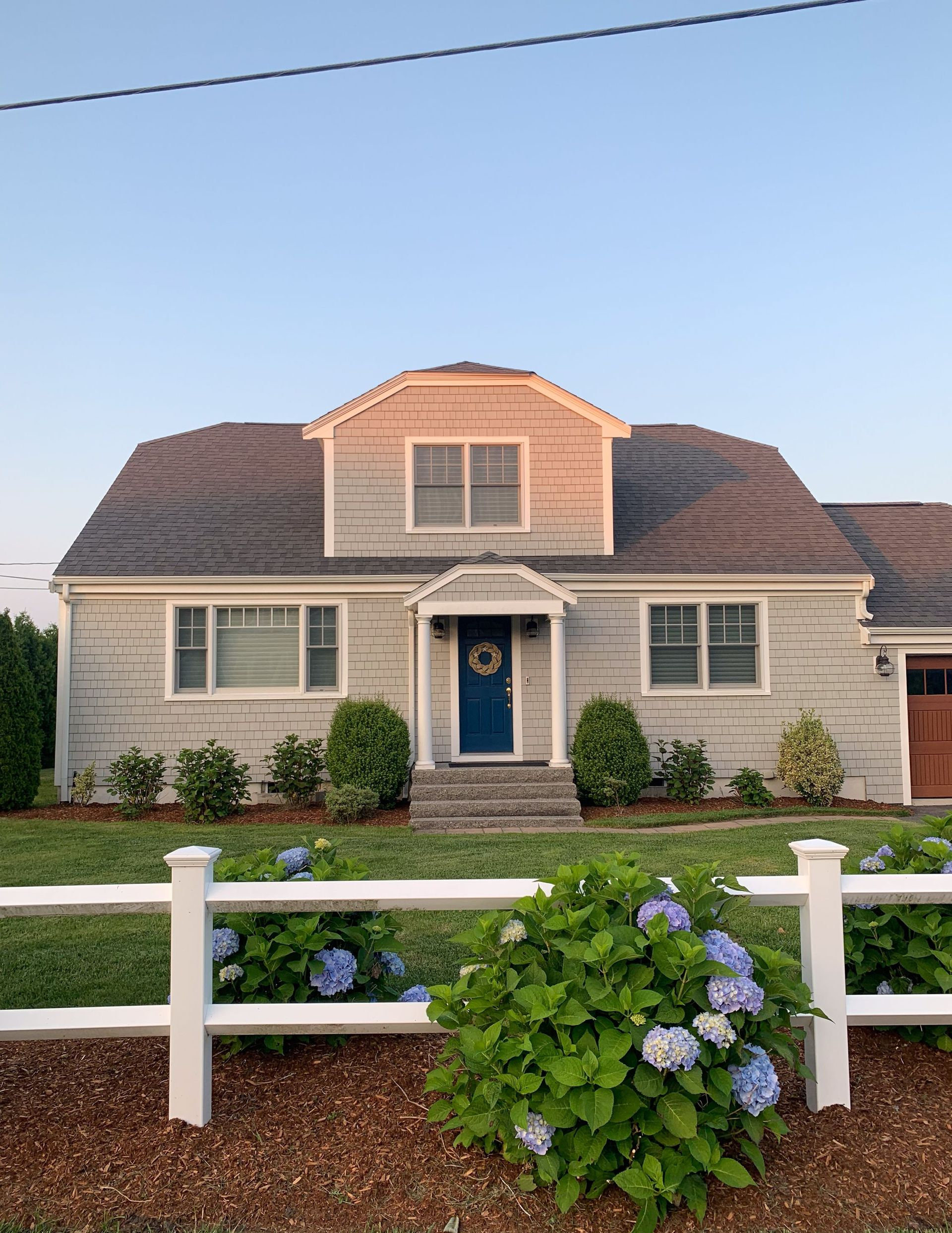 Suburban house with blue door, white fence, and flowering bushes in front yard