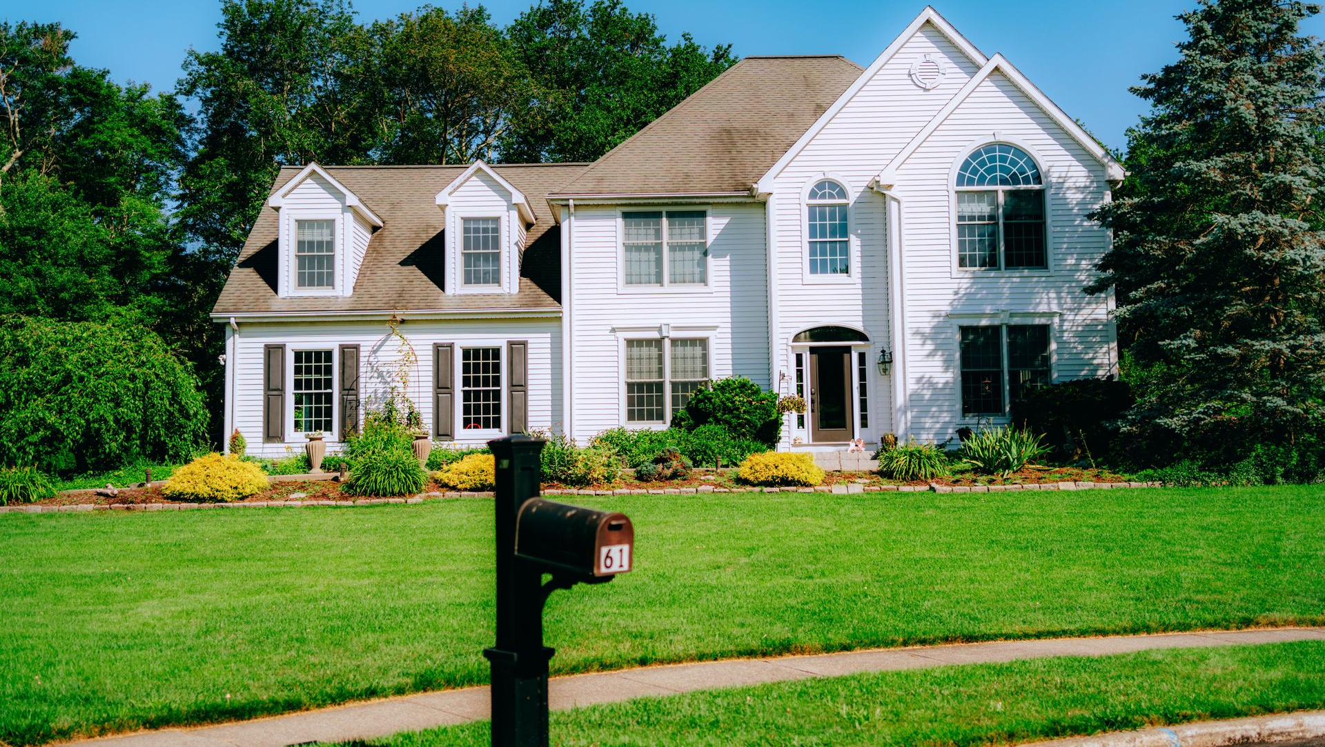 Large white suburban house with a manicured lawn and a black mailbox in front