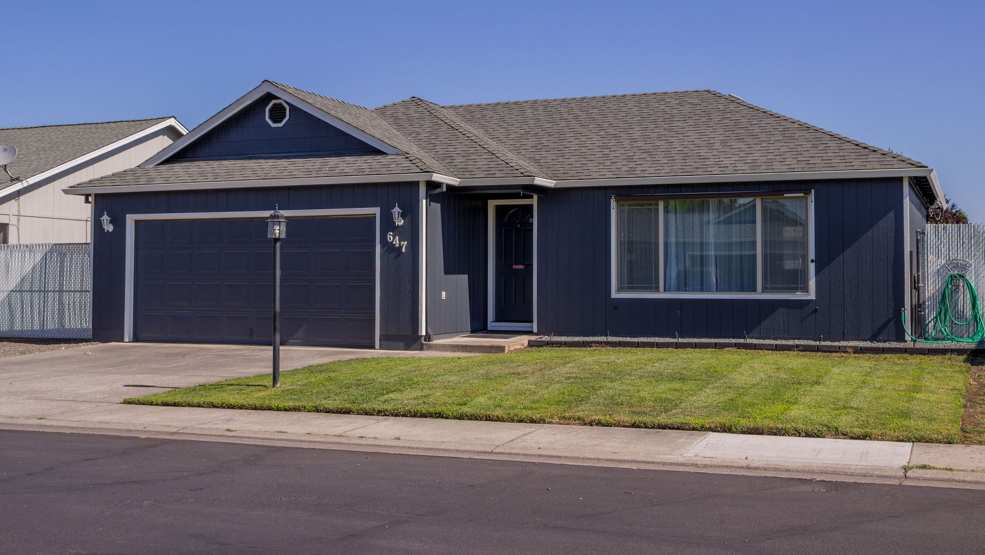 Single-story dark blue house with a two-car garage and front lawn on a suburban street