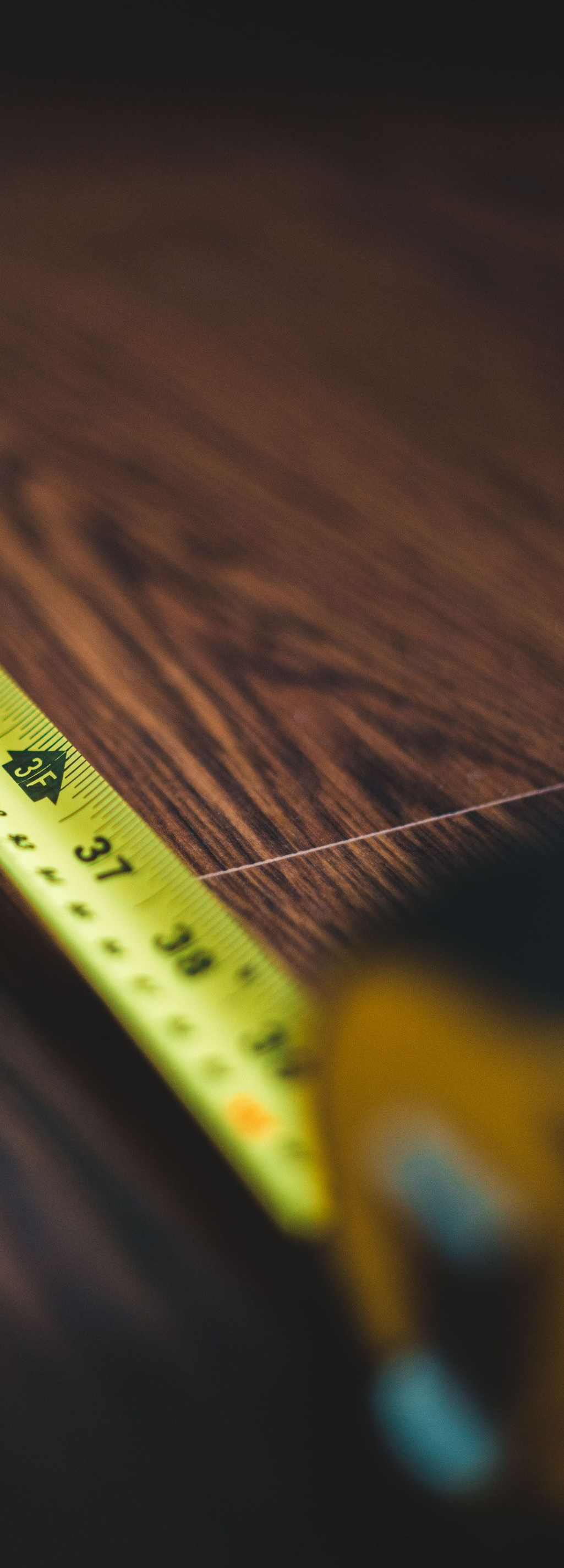 Yellow measuring tape on a wooden surface with visible pencil lines and sawdust