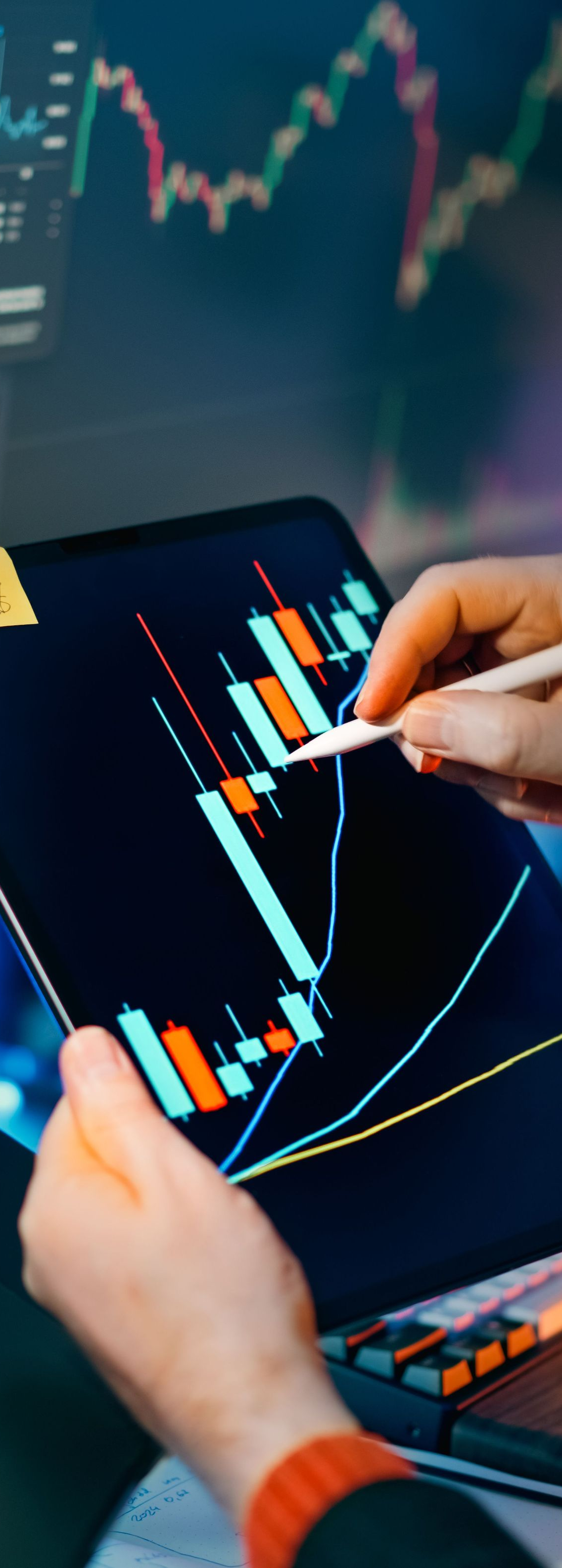 Hands analyzing a glowing candlestick stock chart on a tablet in a dark trading setting