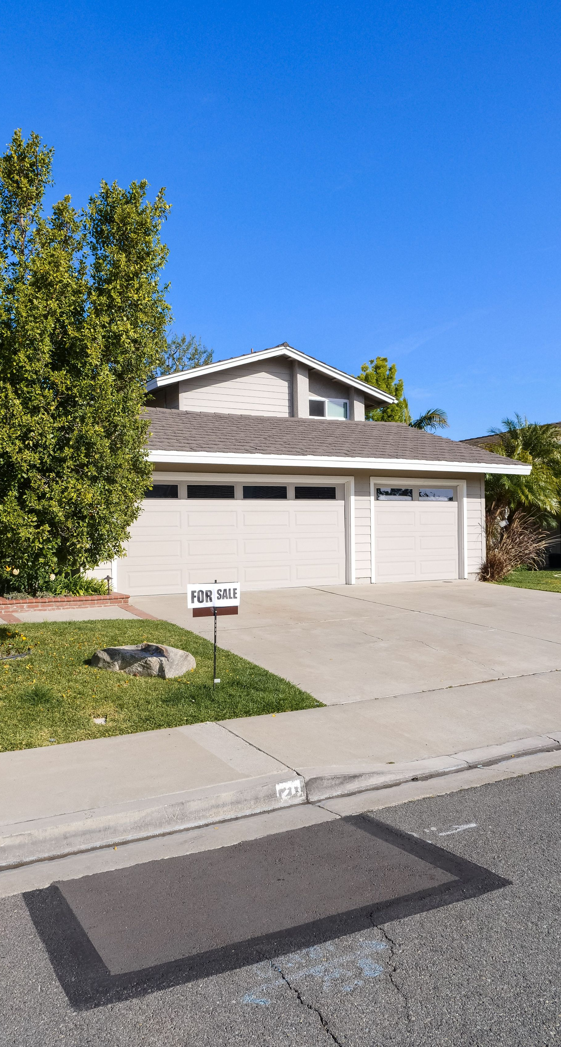 Suburban house with a two-car garage, white stucco exterior, and a driveway under a clear blue sky