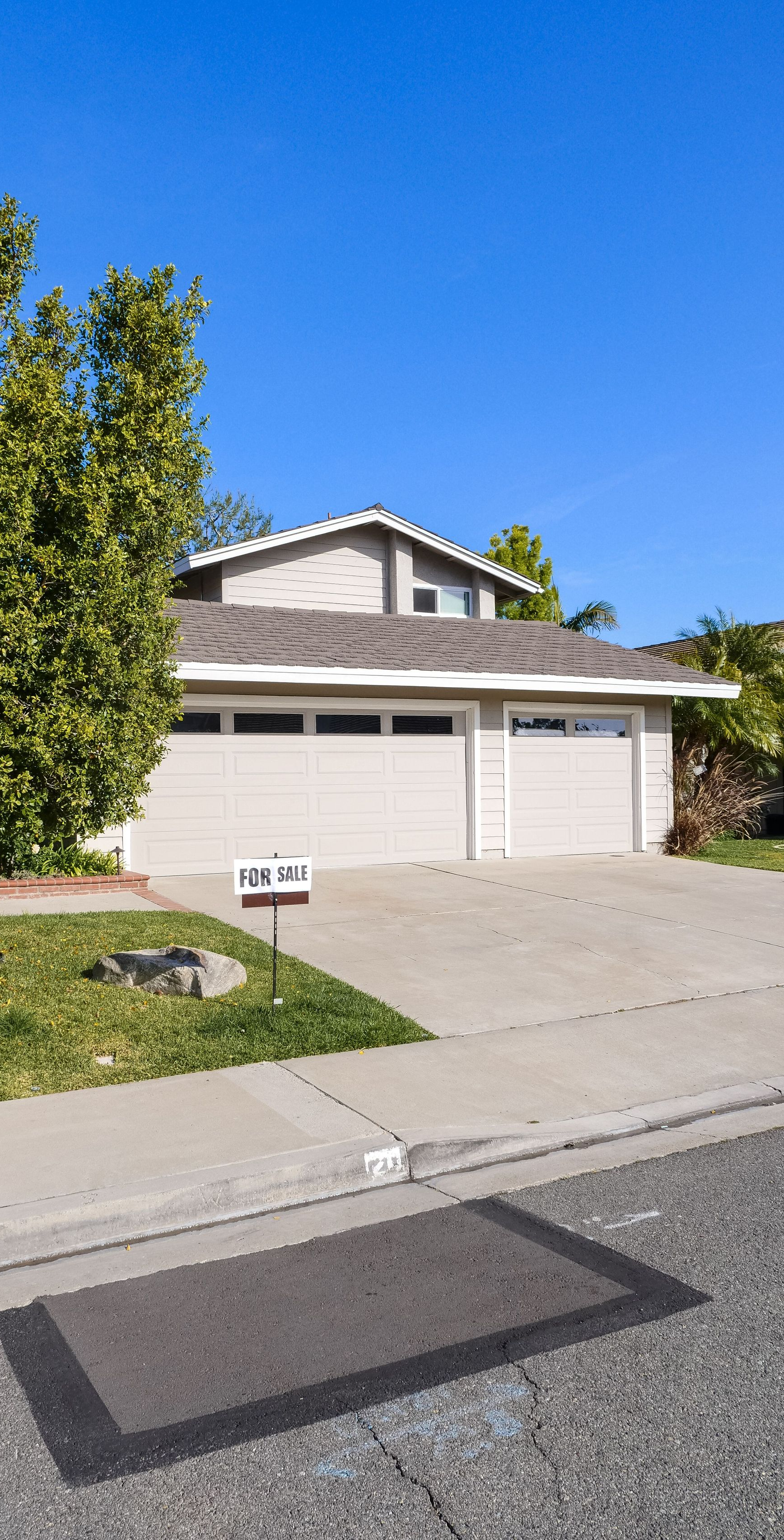 Suburban house with a double garage, driveway, and tree under a clear blue sky