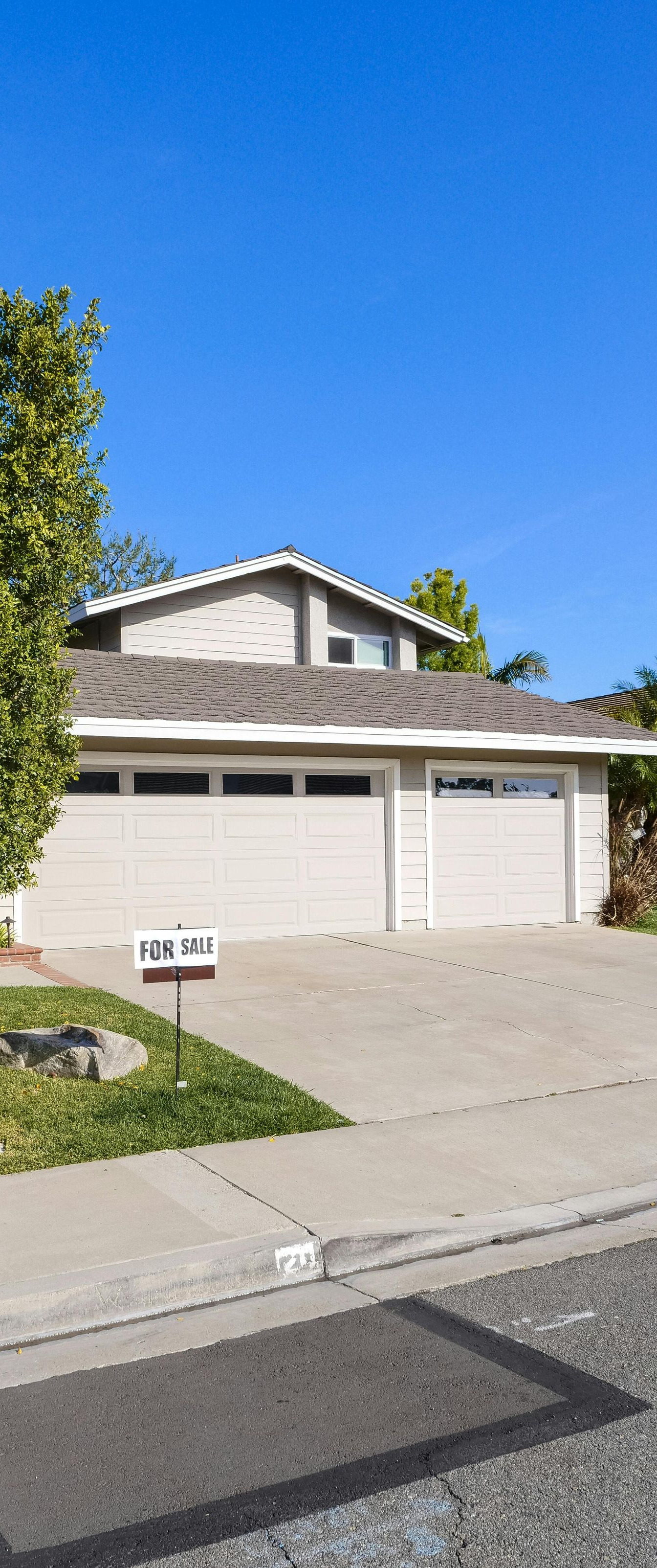 Two-story house with a light-colored garage, driveway, and tree in front against a blue sky.
