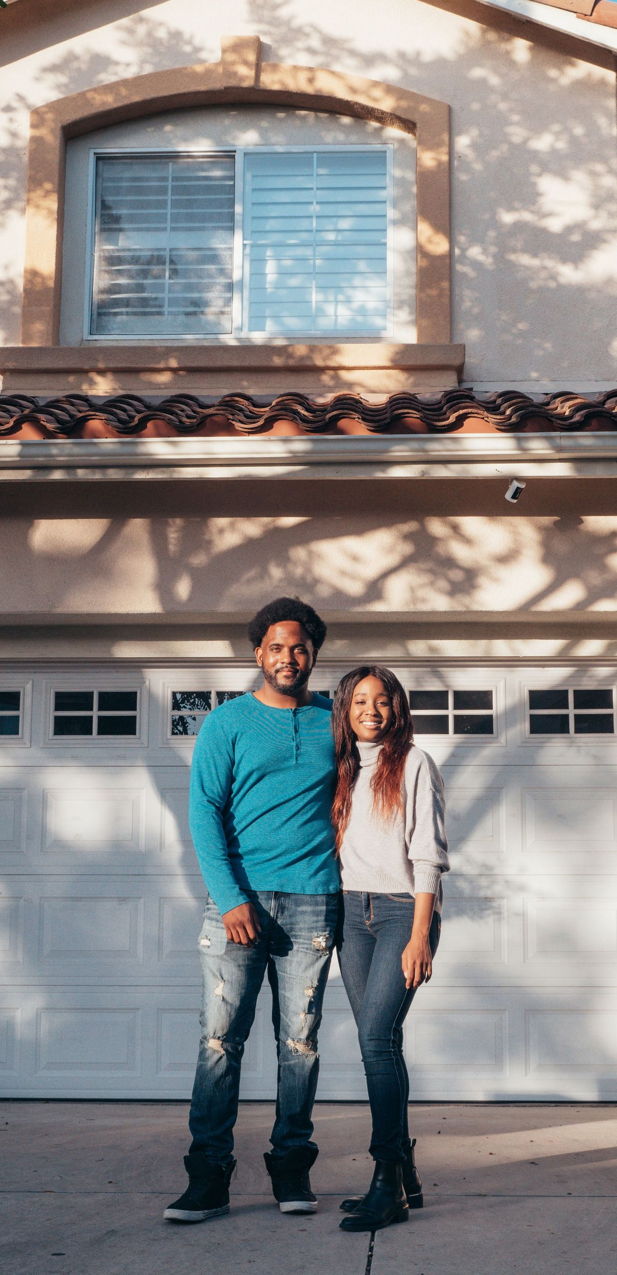 Two people standing in front of a white garage door on a sunny suburban street