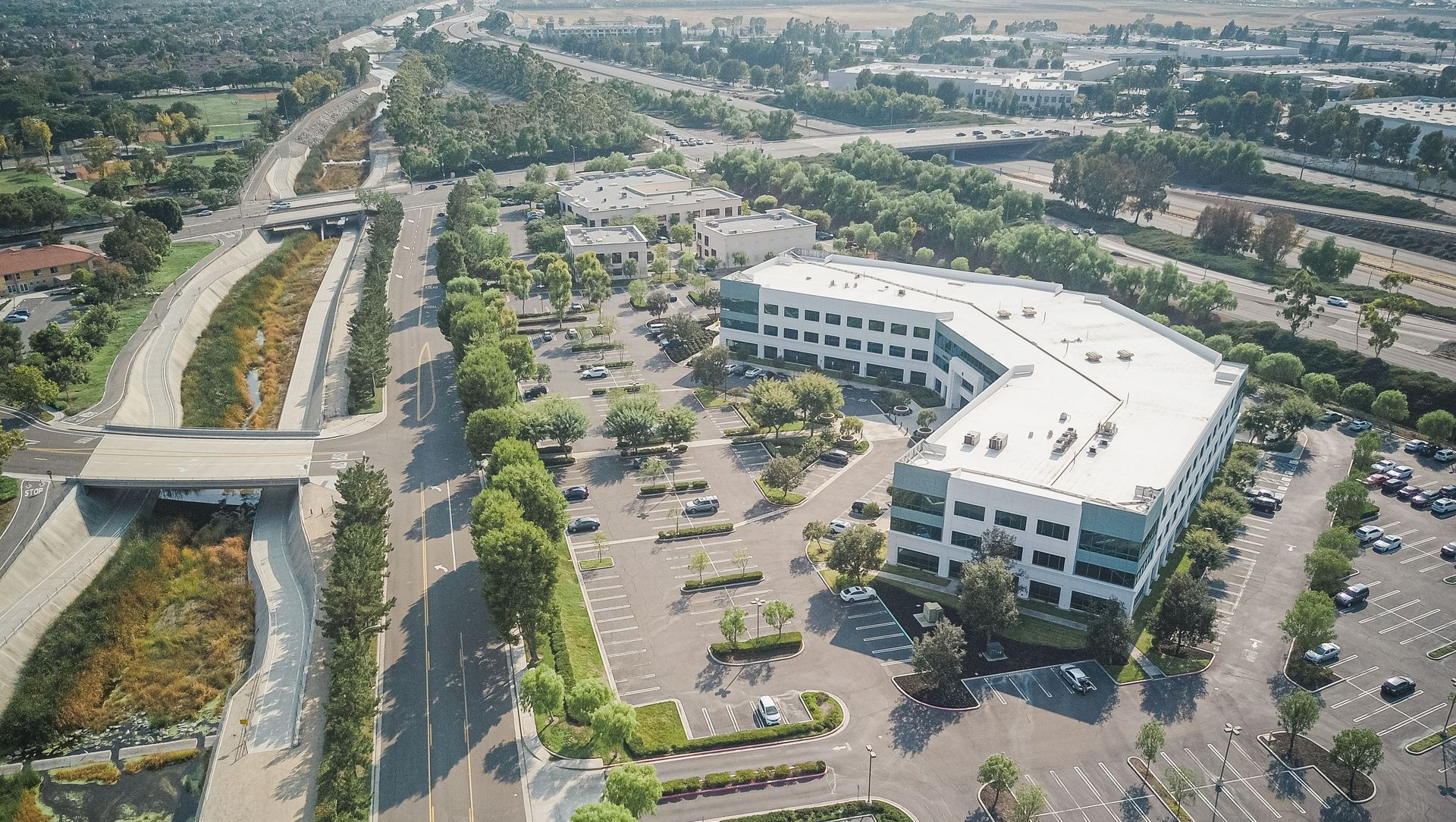 Aerial view of a modern office building with a parking lot and surrounding roads in a suburban area