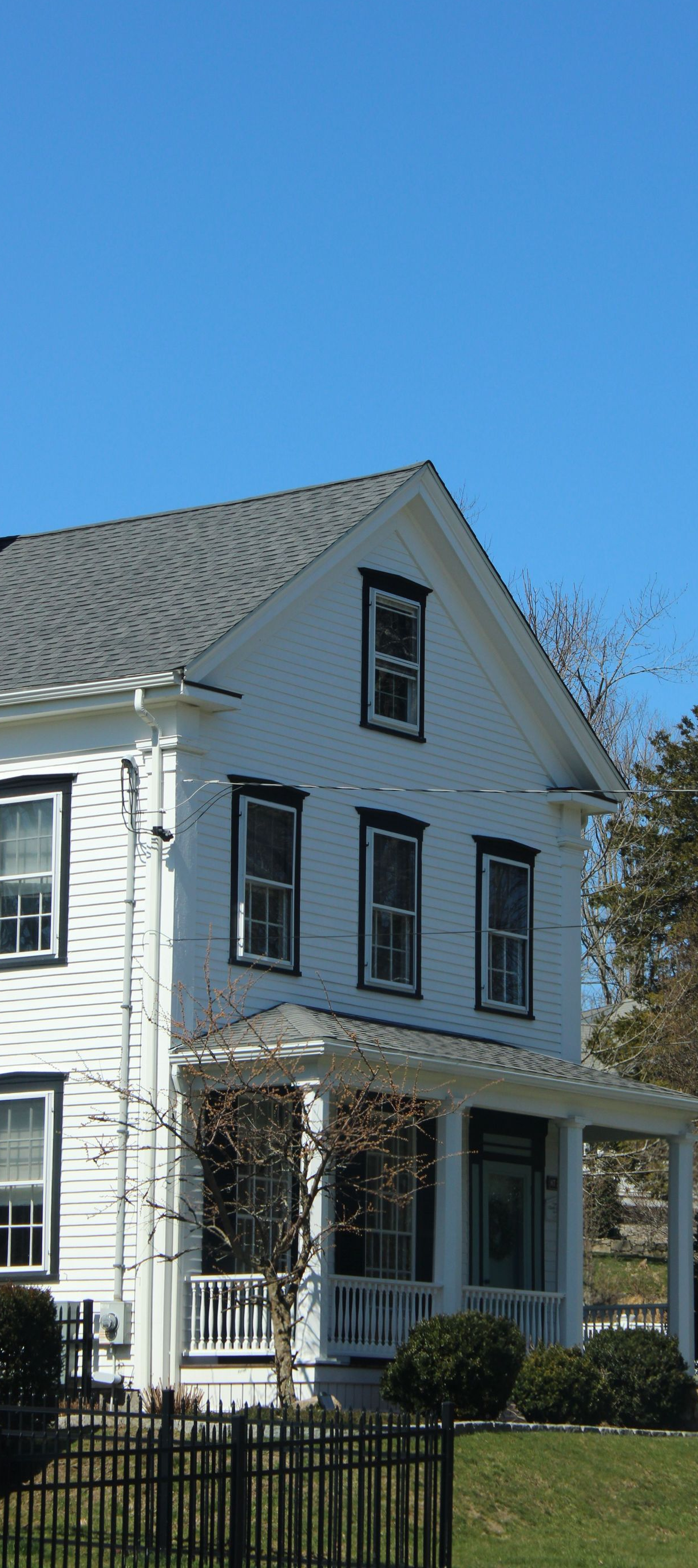 White two-story house with gray roof and front porch behind a black fence under a clear blue sky