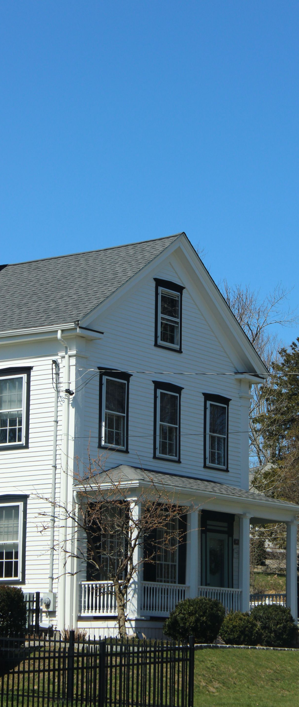 White two-story house with black shutters and a brick chimney under a clear blue sky