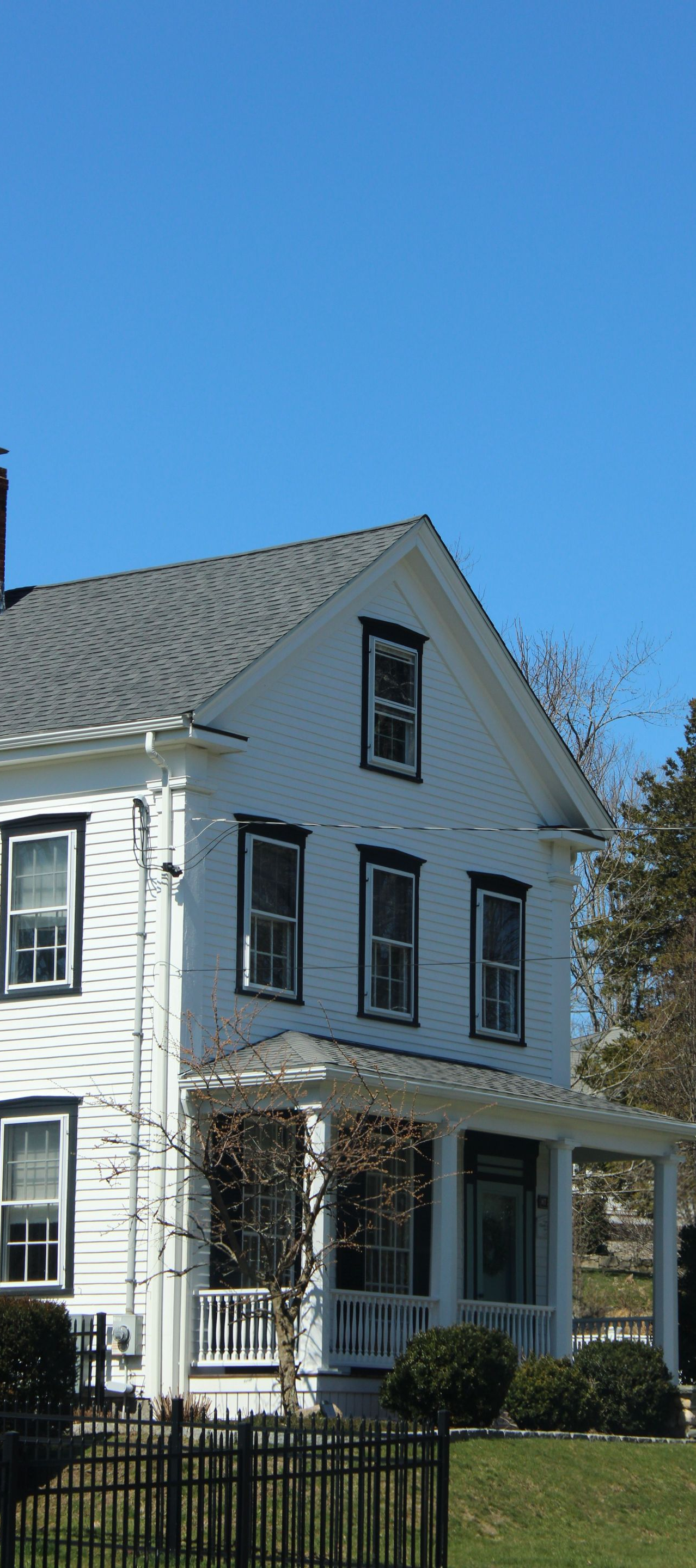 White two-story house with black shutters and a porch under a clear blue sky