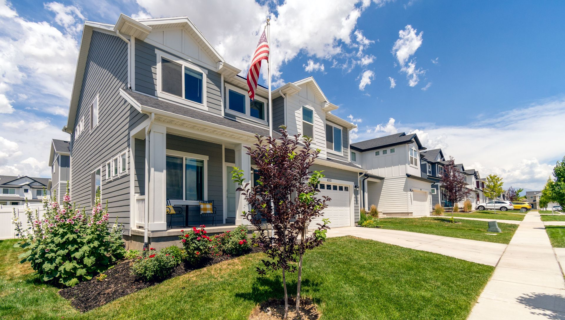 Suburban house with gray siding, front lawn, sidewalk, and an American flag under a blue sky.