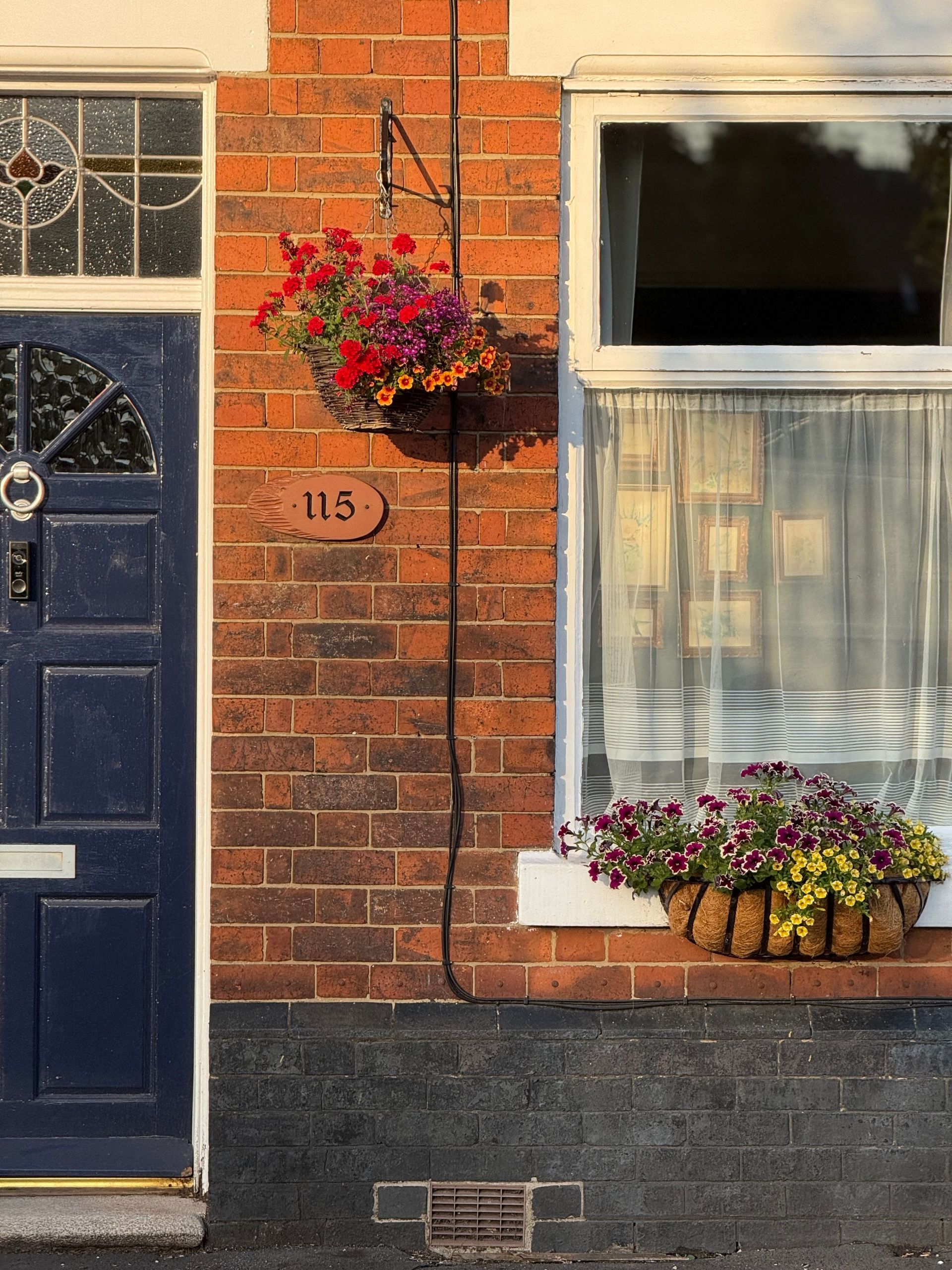 Brick house facade with blue door, window, and flower baskets beside the doorway