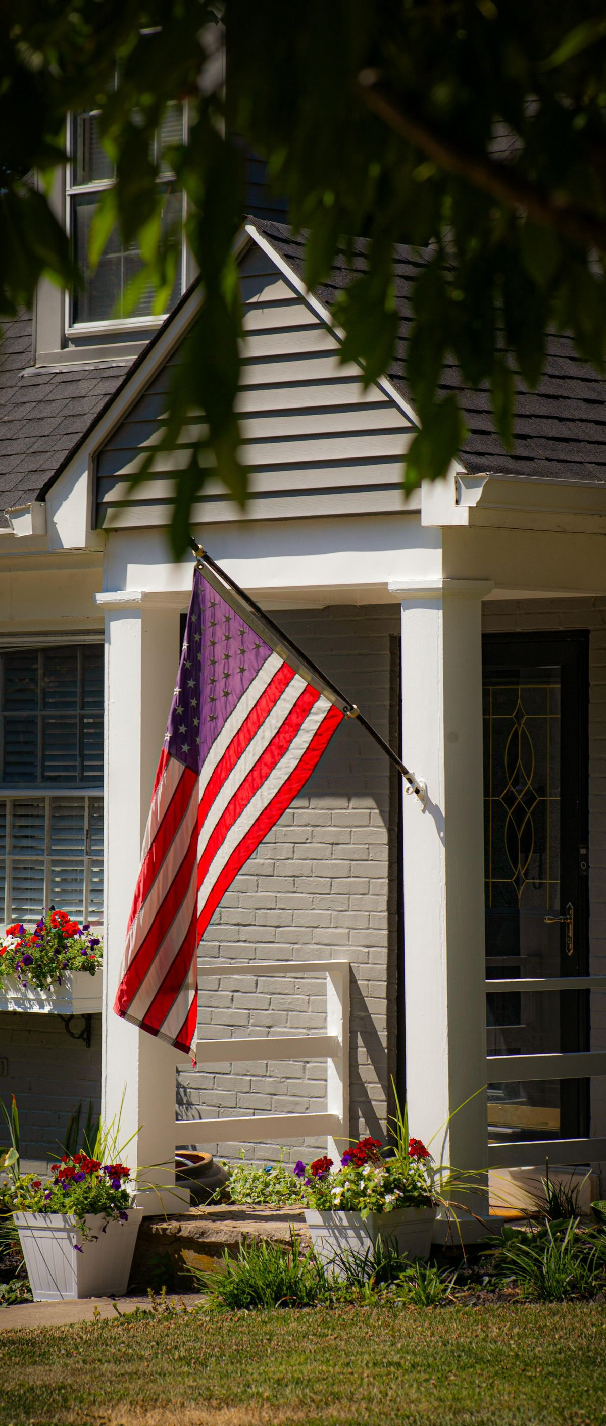American flag on a porch of a beige house with white columns and flower boxes
