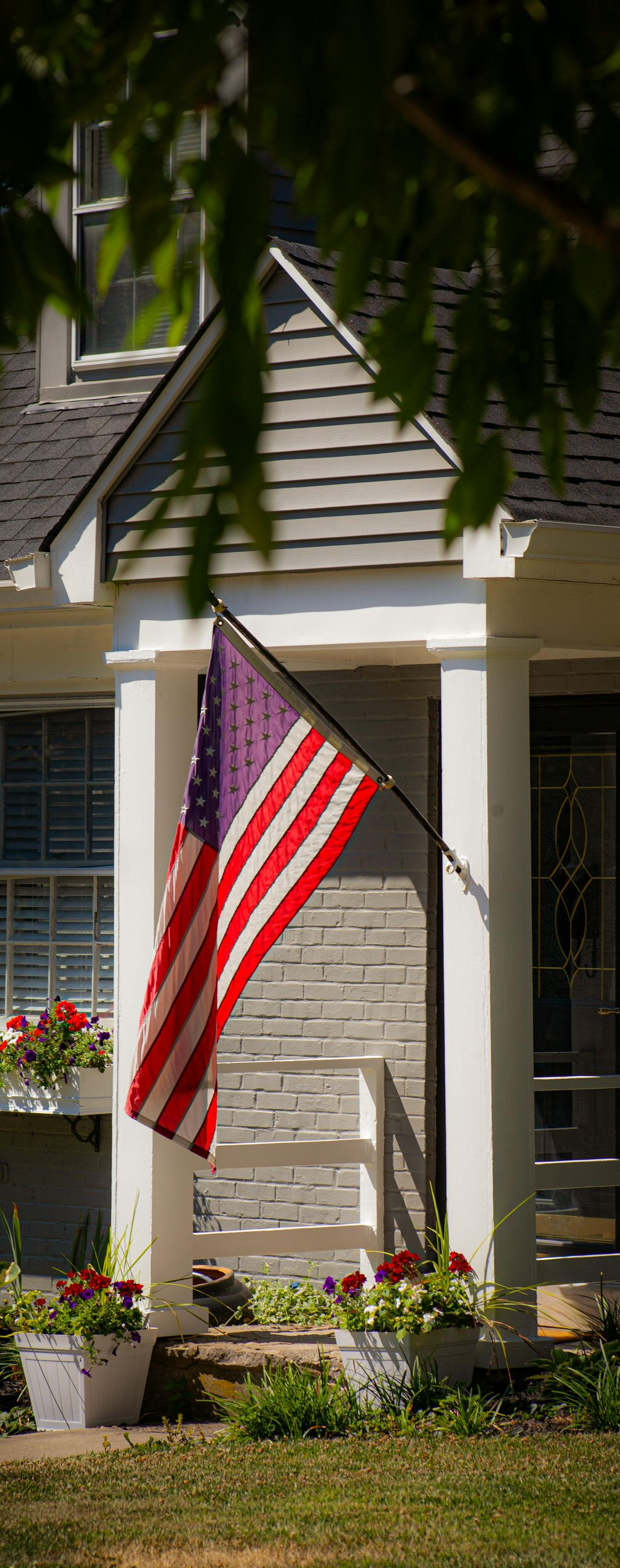 American flag hanging from a house porch with white columns and flower boxes