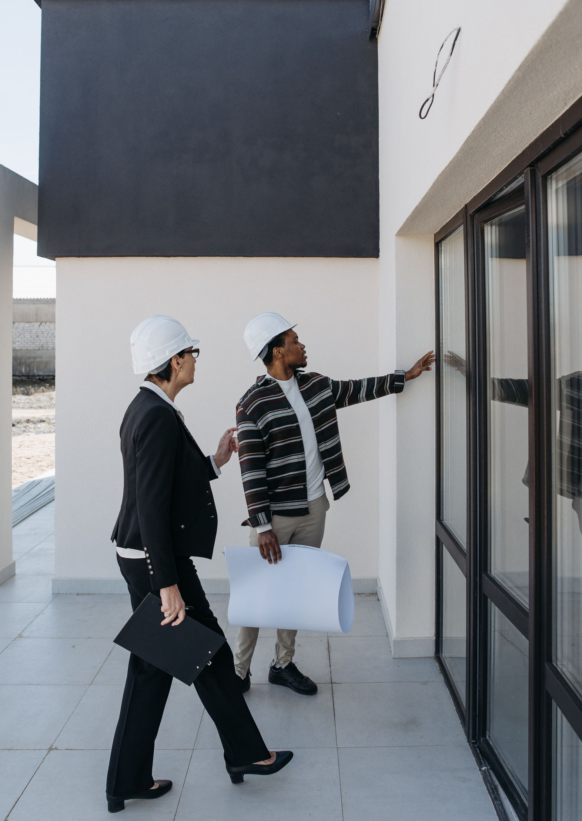 Two people in hard hats inspecting a building entrance, one pointing at the glass door.