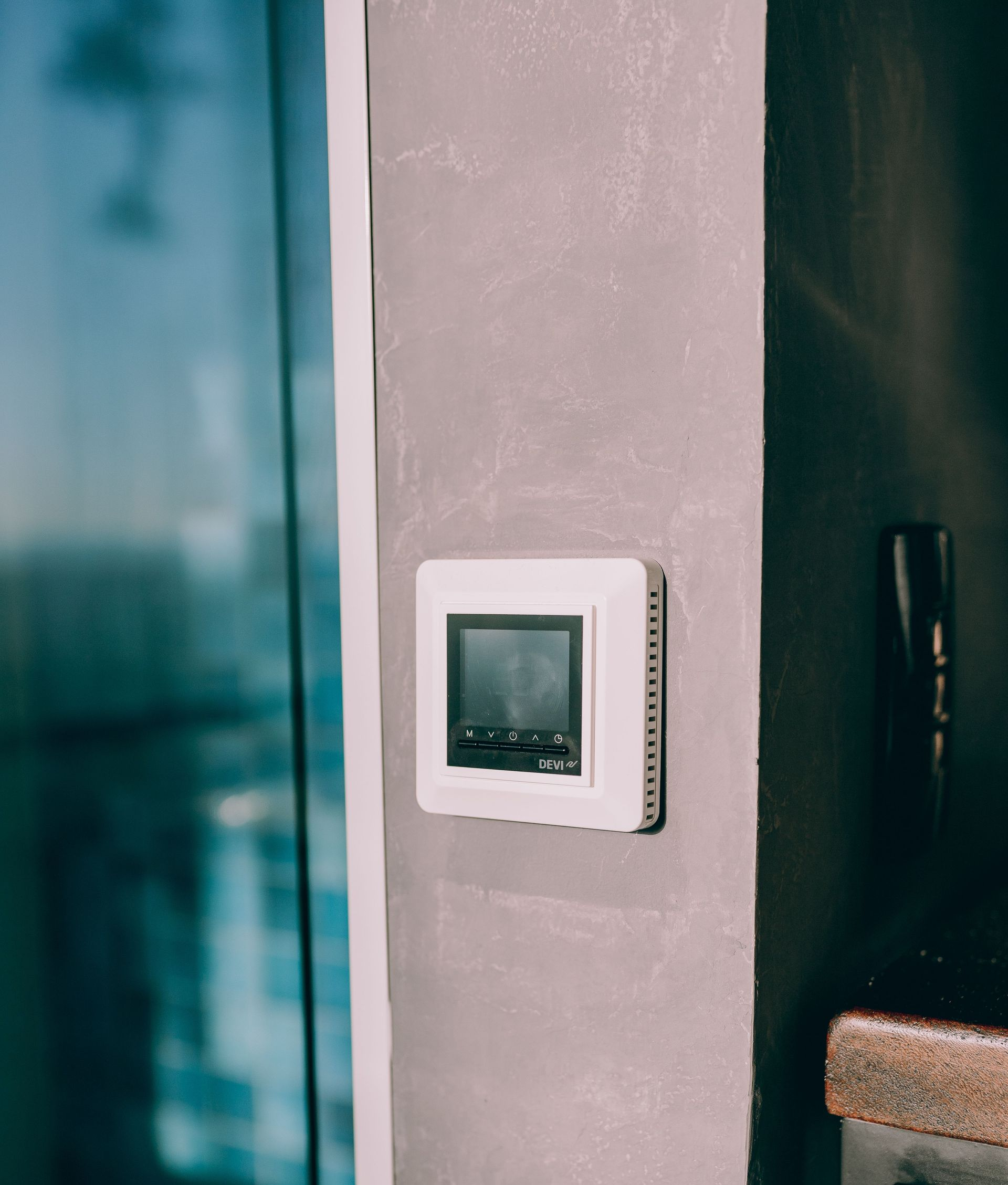 Wall-mounted thermostat on a gray wall beside a dark doorway.