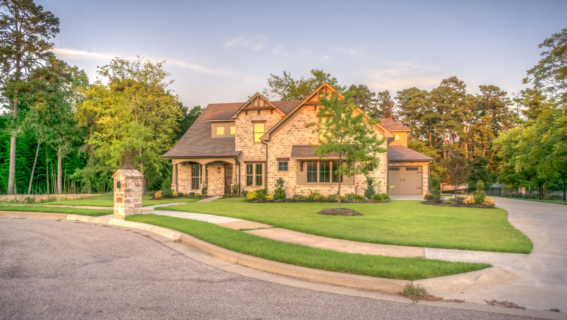 Large stone house with a landscaped lawn and driveway at sunset
