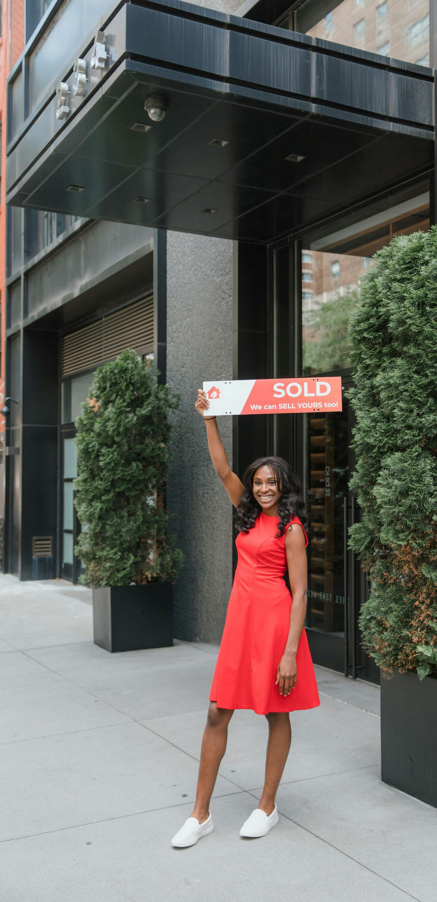 Woman in red dress holding a sign outside a building entrance with tall planters