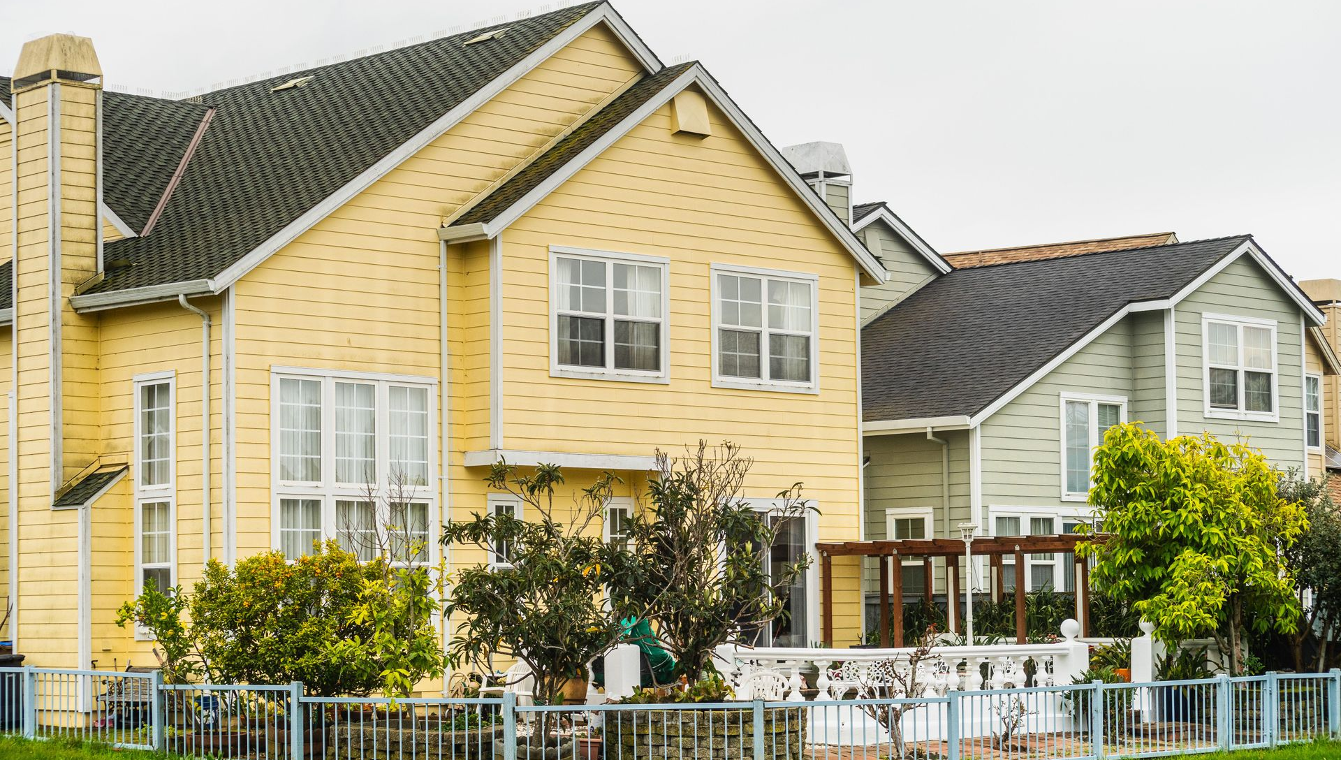 Yellow suburban houses with white trim and fenced front yards under cloudy skies