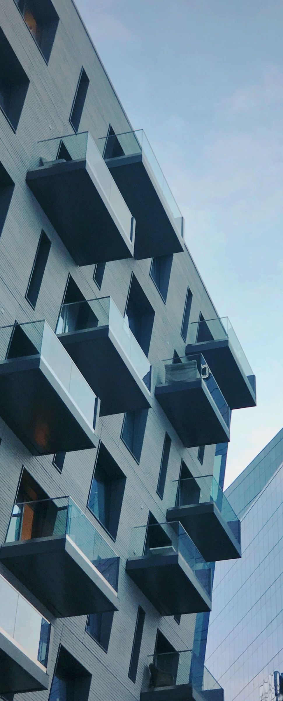 Tall modern apartment building with blue-gray balconies against a pale sky