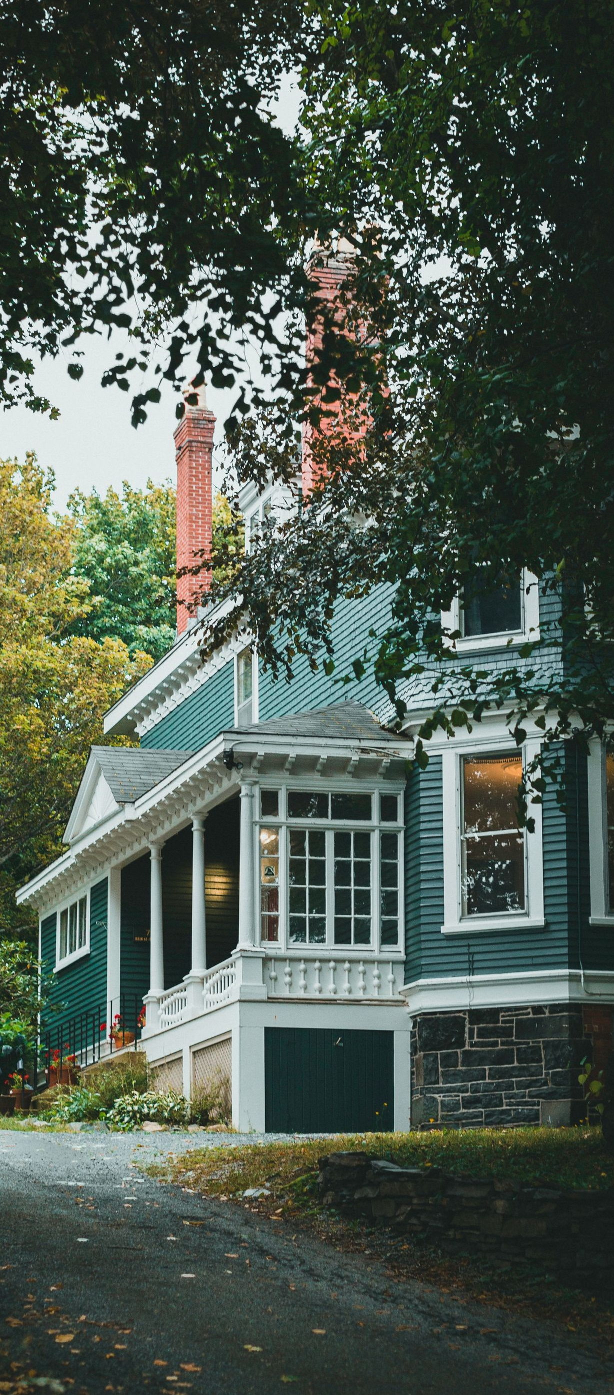 Victorian house with white trim and red chimneys, framed by trees along a quiet roadside