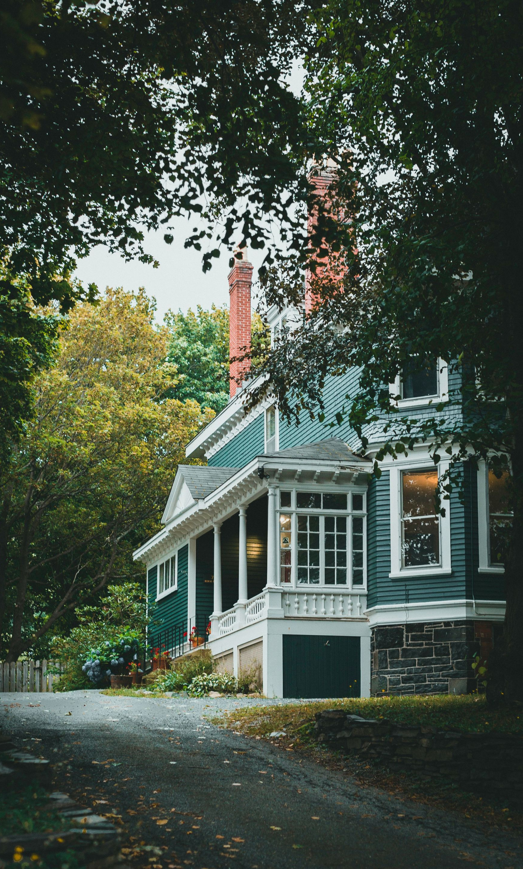 Tree-lined driveway beside a white Victorian house with a porch and red chimney