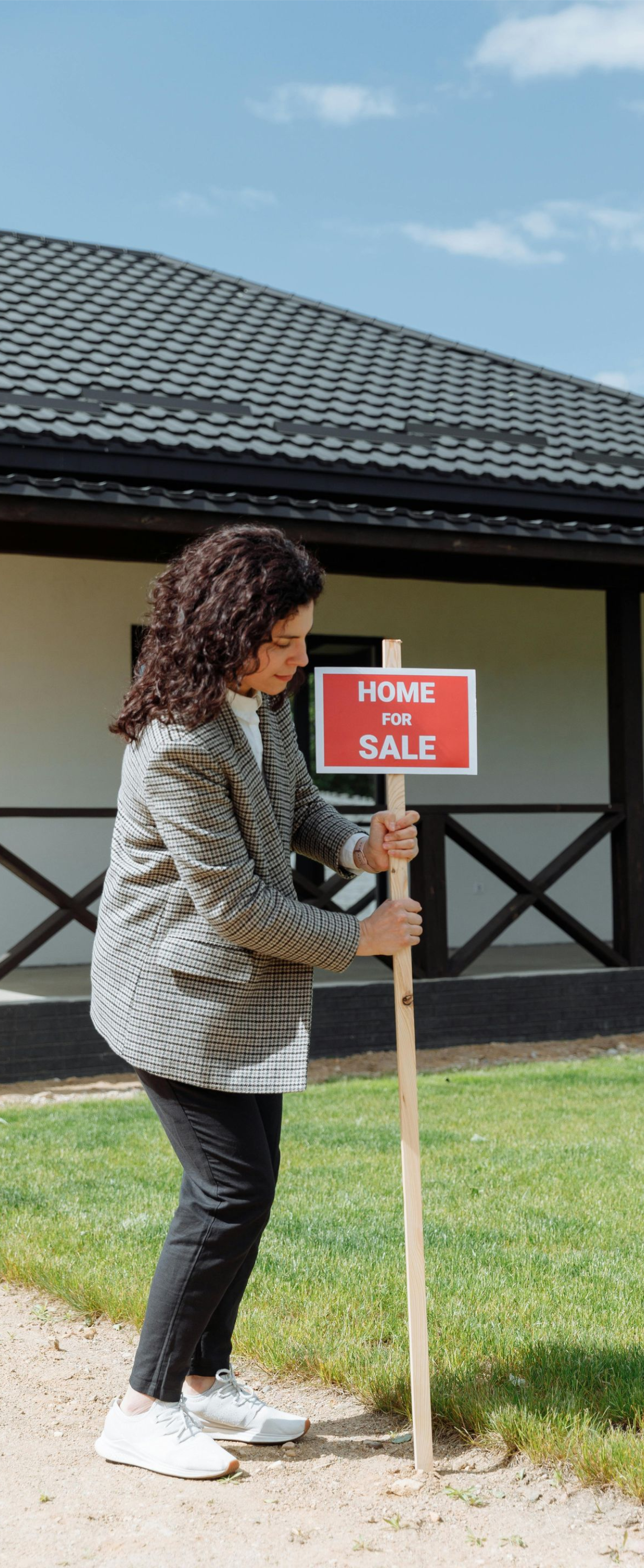 Person planting a red “Home for Sale” sign in a front yard near a house