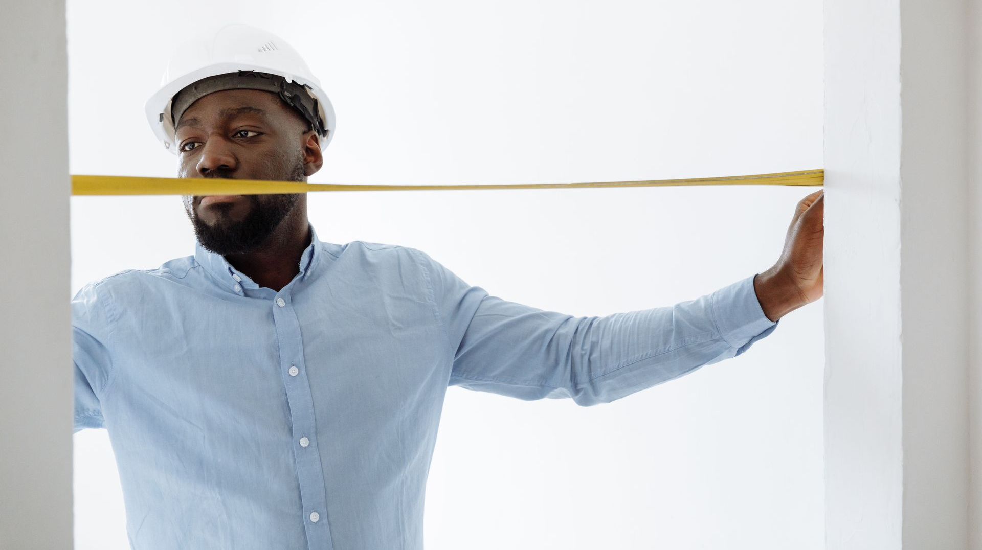 Construction worker stretching a yellow measuring tape across a white wall