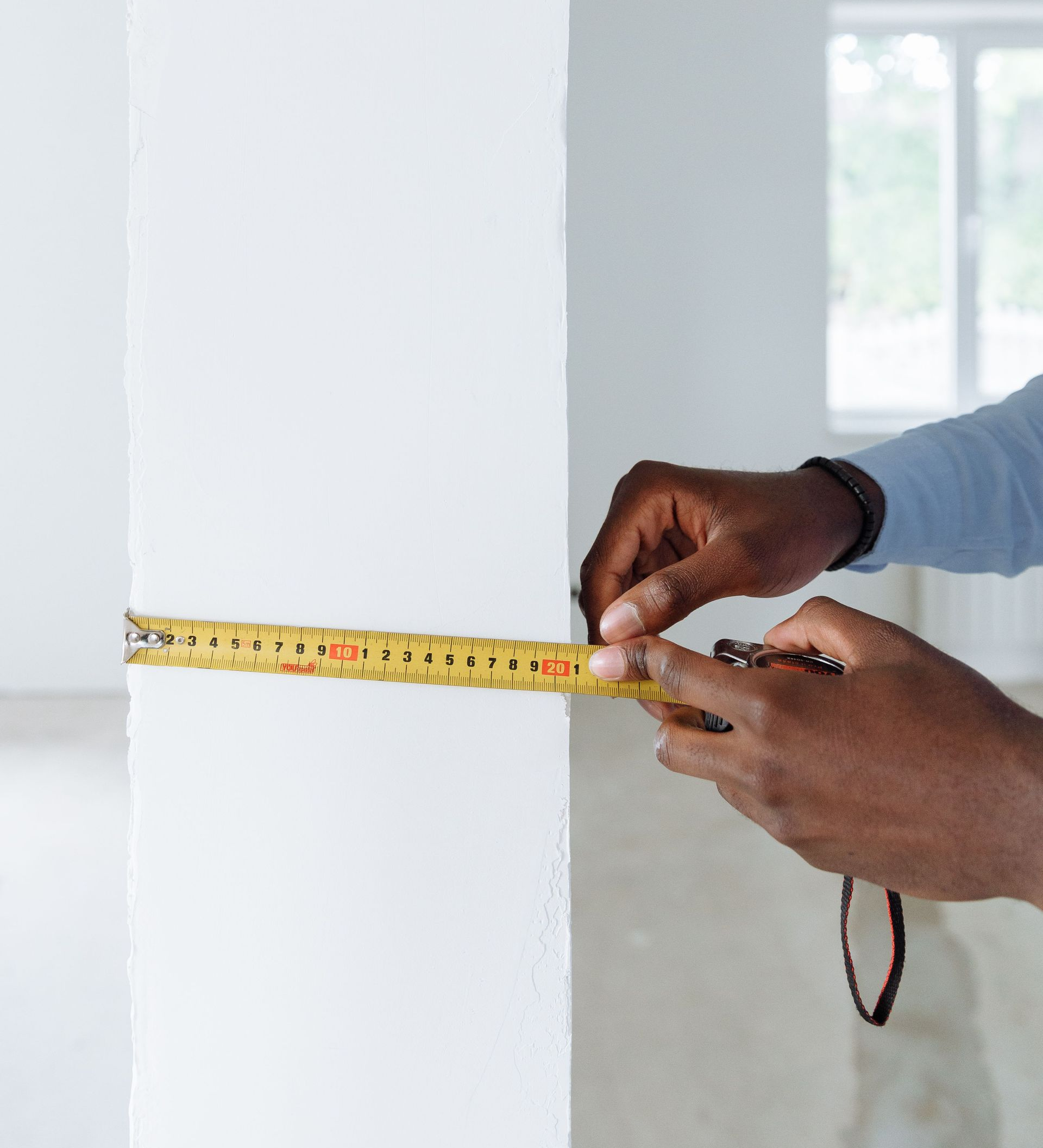 Hands measuring a white wall with a yellow tape measure