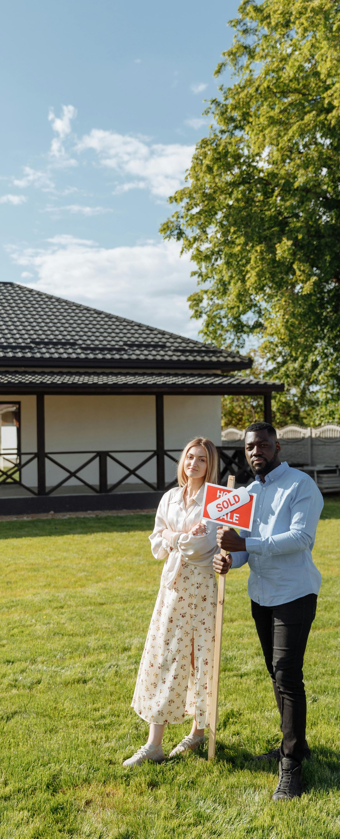 Two people standing on a grassy lawn in front of a house, looking at a phone under bright sunlight.