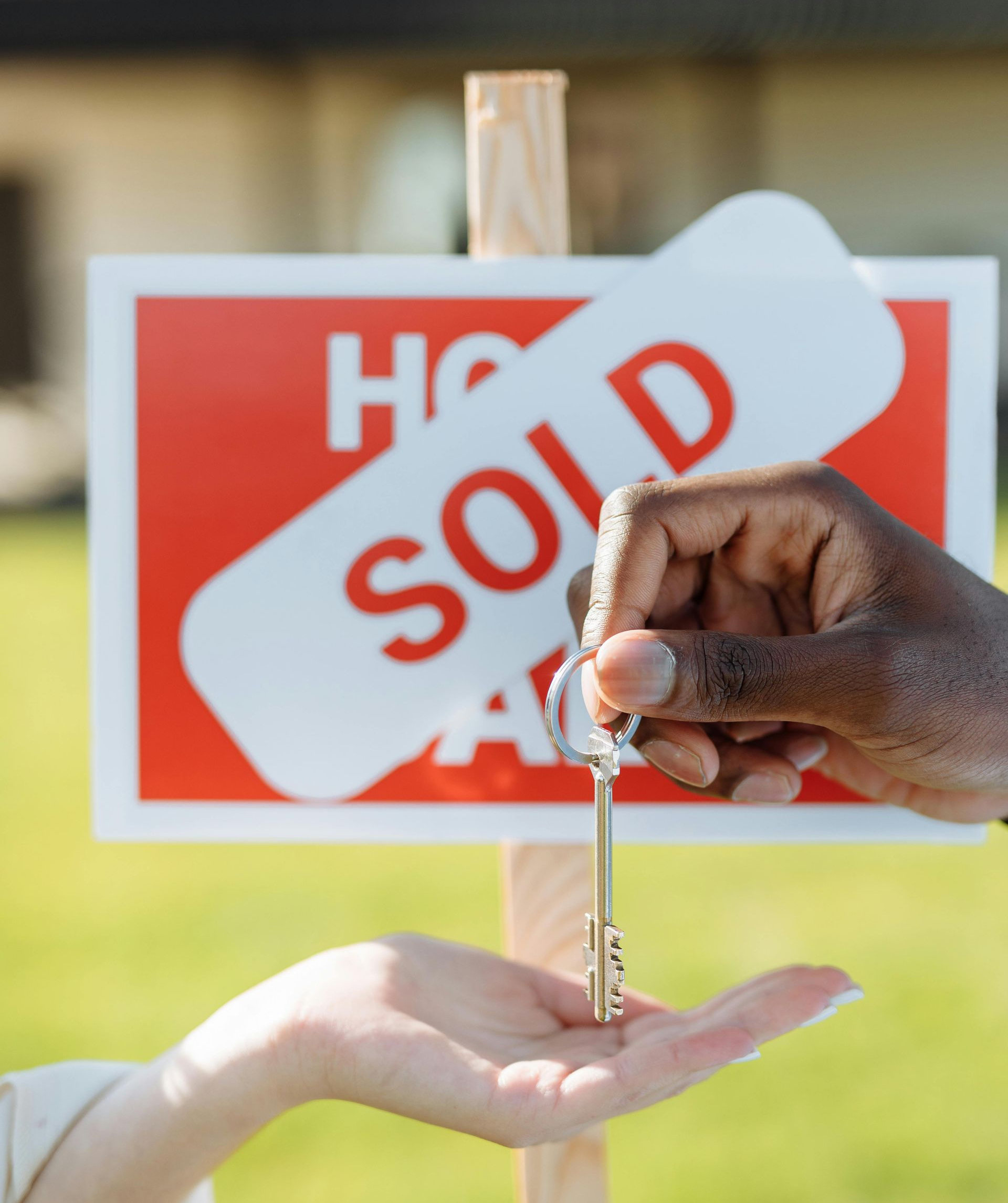 Hand holding a set of keys in front of a small wooden house cutout.