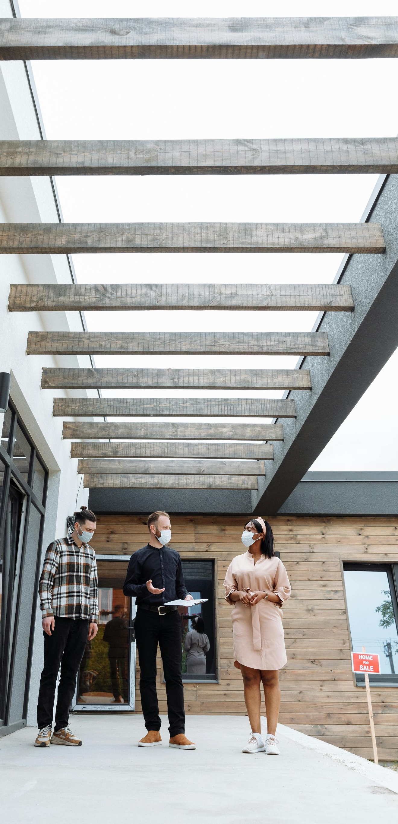 Three people walking under a modern outdoor pergola outside a building