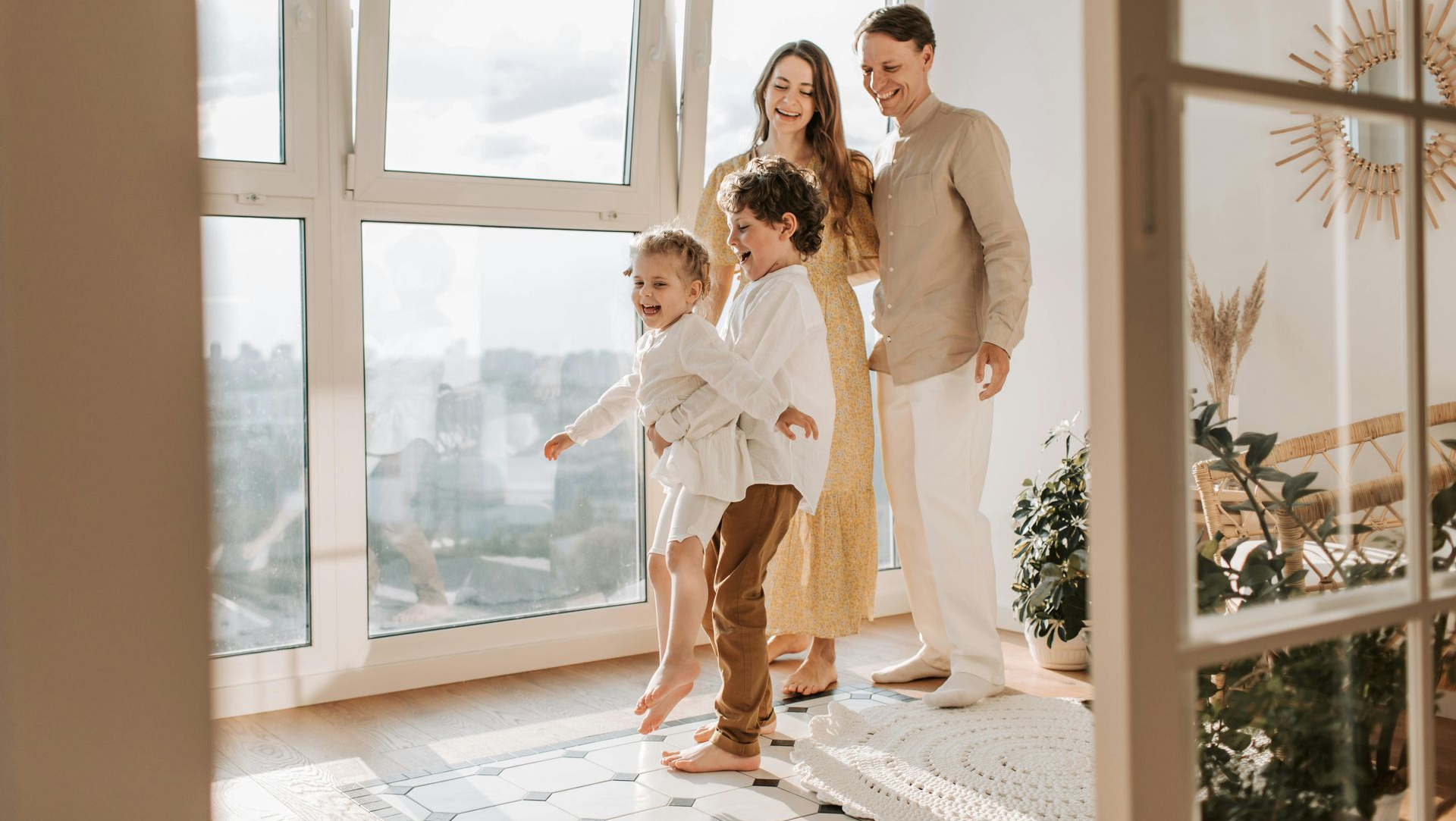 Family of four standing by large sunlit windows in a bright room