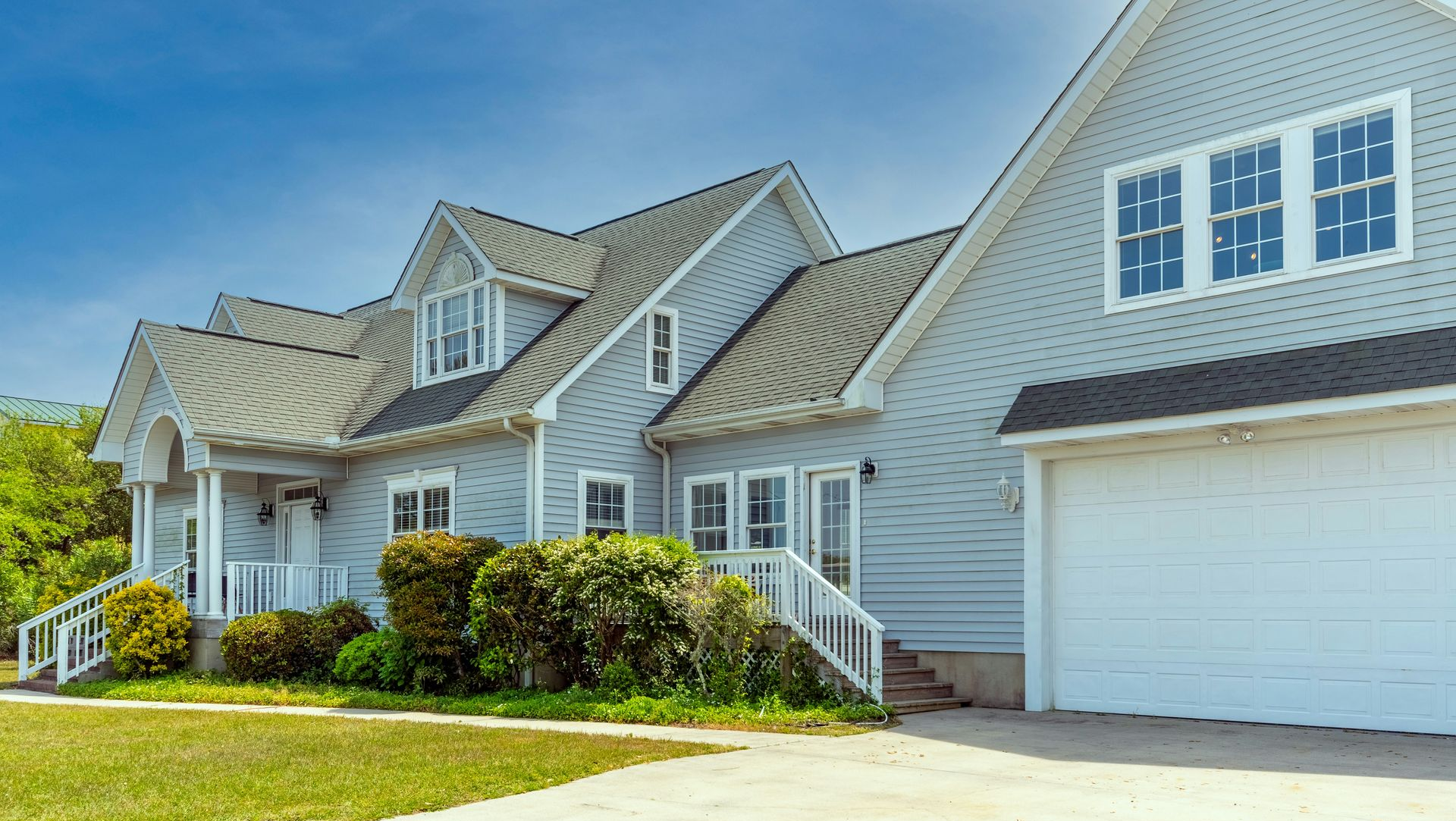 Suburban gray house with white trim, front porch, garage, and green lawn on a sunny day