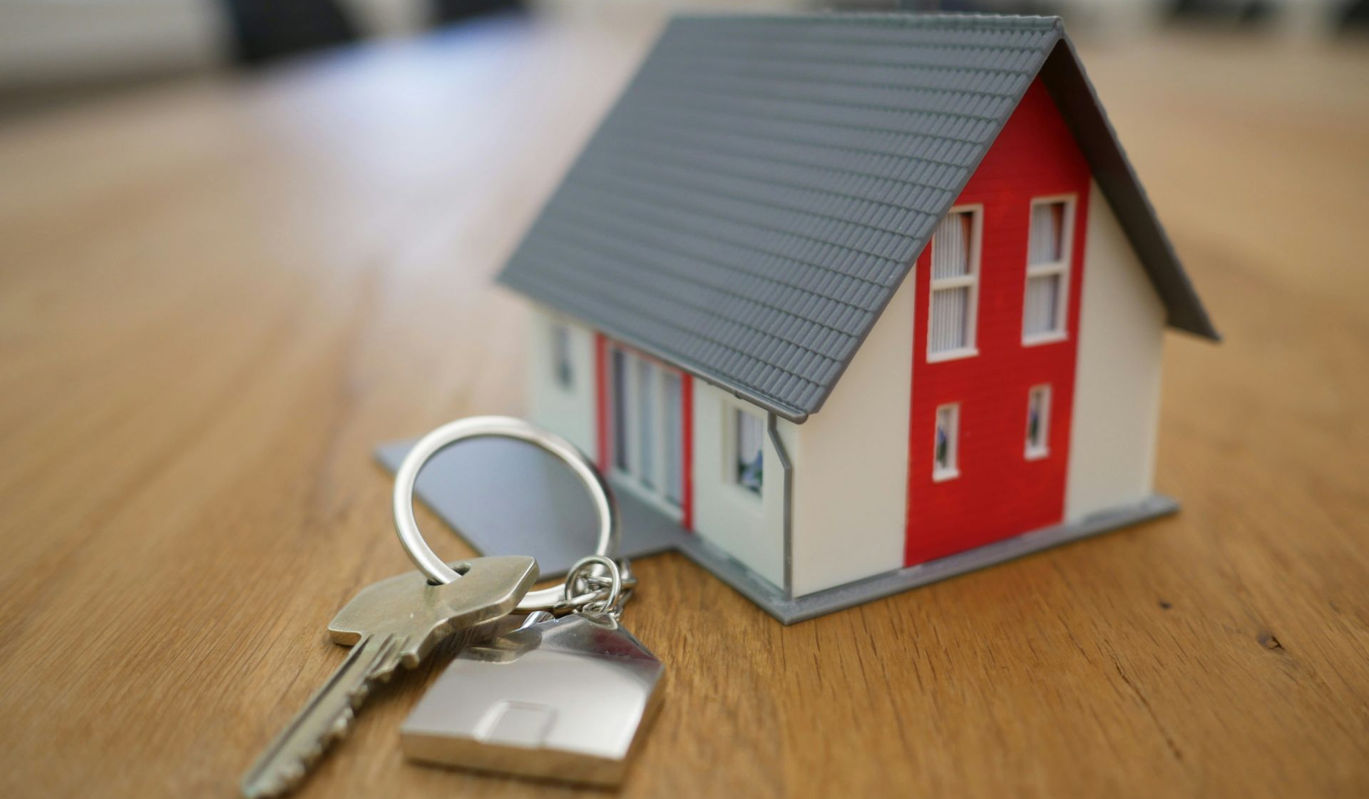Small model house with keys on a wooden table, suggesting home purchase or real estate.