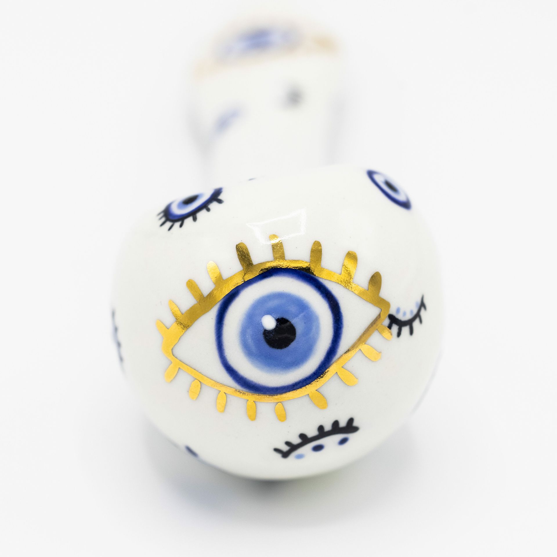 A white ceramic pipe decorated with several blue evil eye symbols, one prominently outlined in gold.