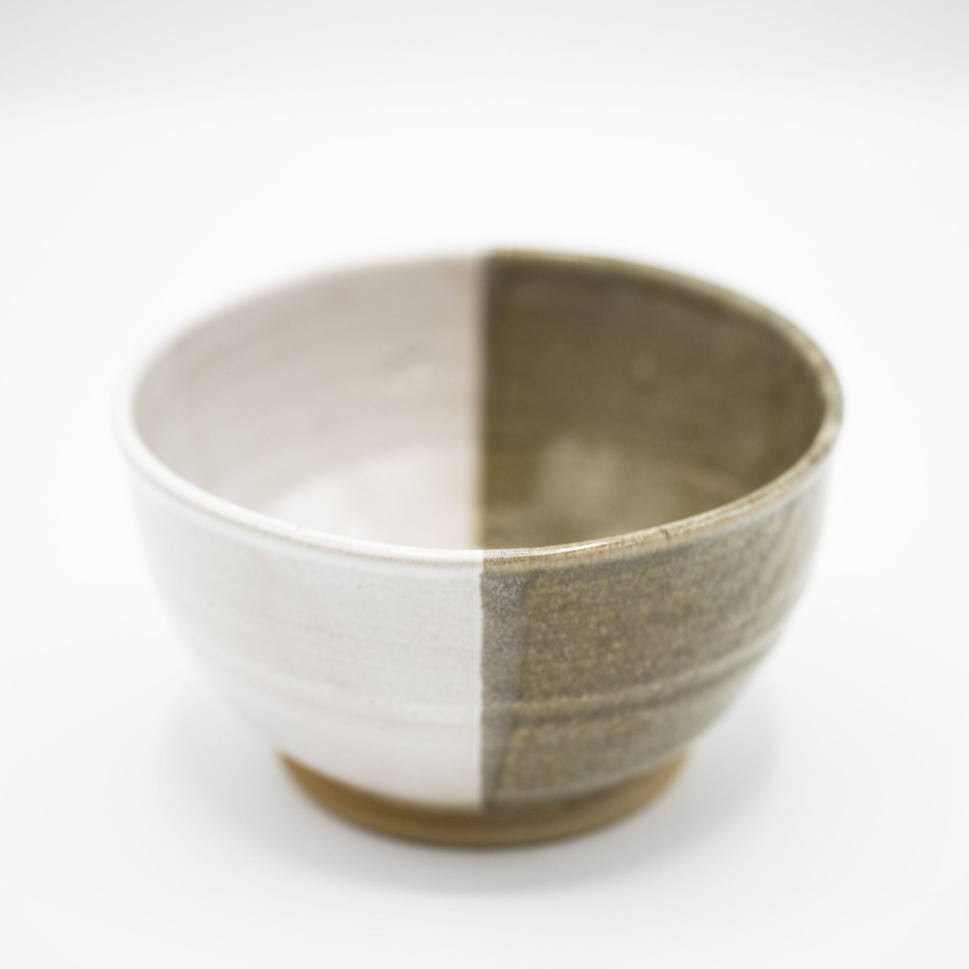 A handmade ceramic bowl with a clean split design, one half matte white and the other half earthy, textured olive green.