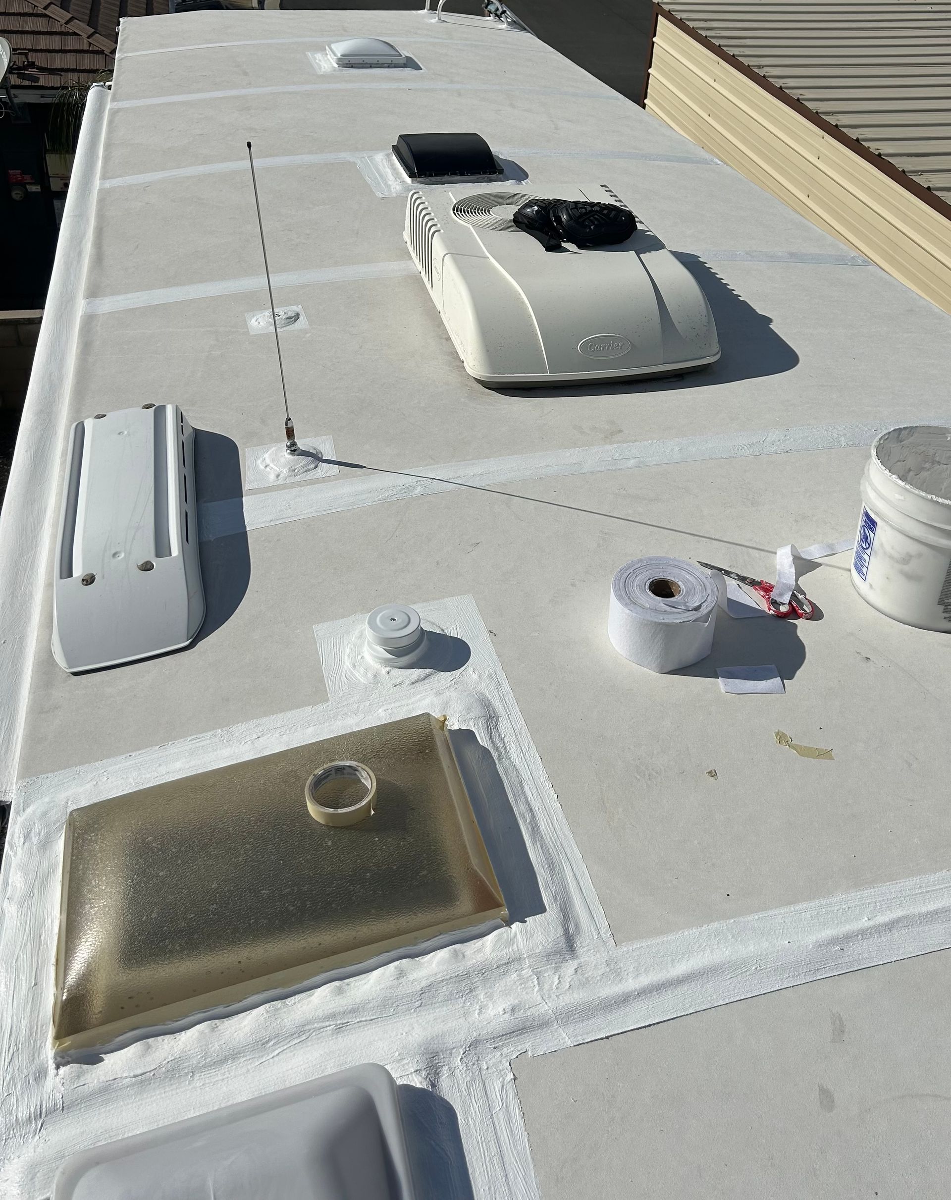Flat white rooftop with vents, skylights, and a white HVAC unit in bright sunlight.