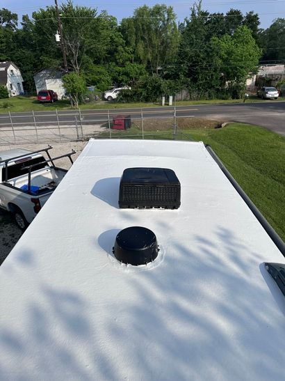 RV roof with black vent and round fan cover, overlooking a tree-lined residential street.