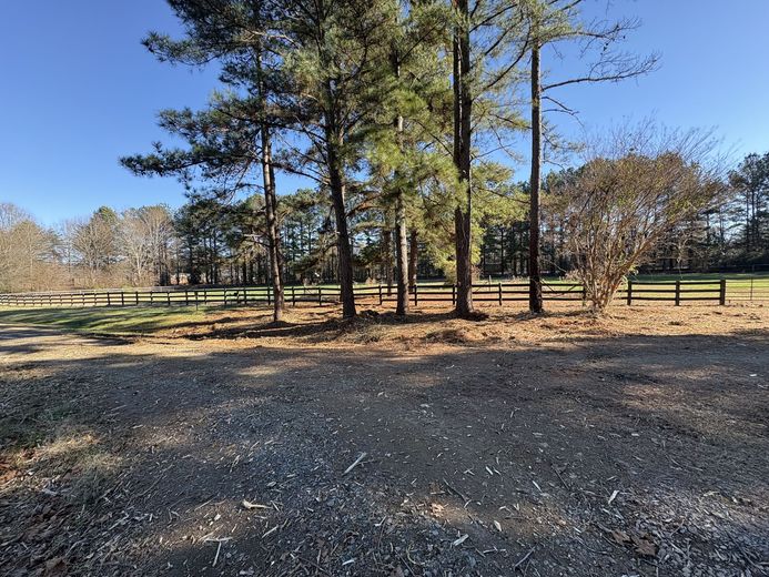 A dirt road surrounded by trees and a fence on a sunny day.