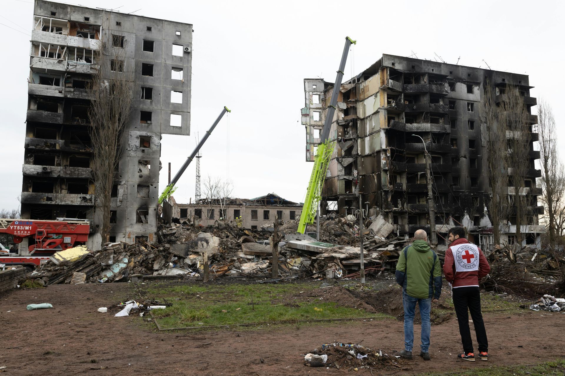 Two men are standing in front of a ruined building.