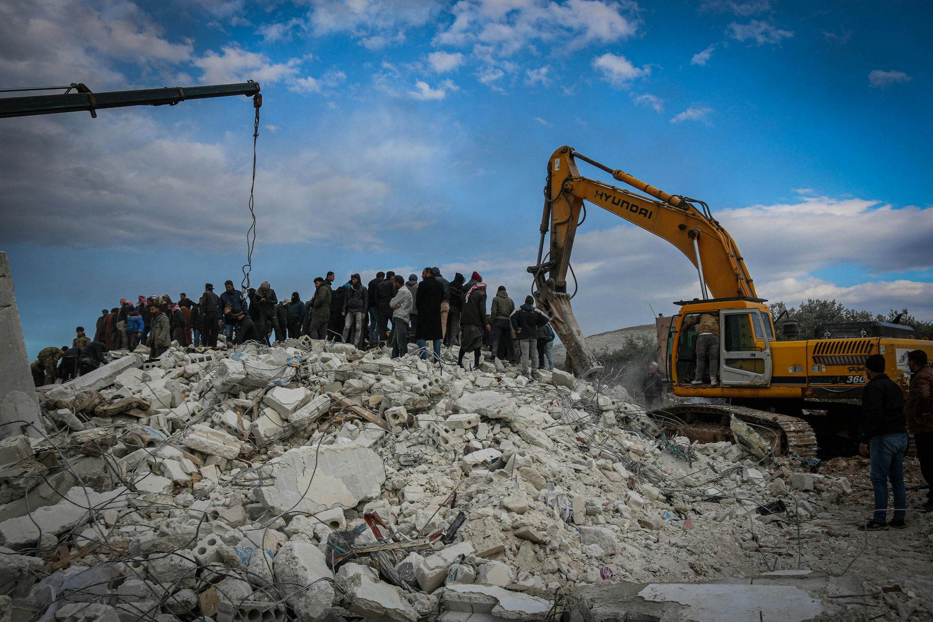 A large pile of rocks is being demolished by a yellow excavator.