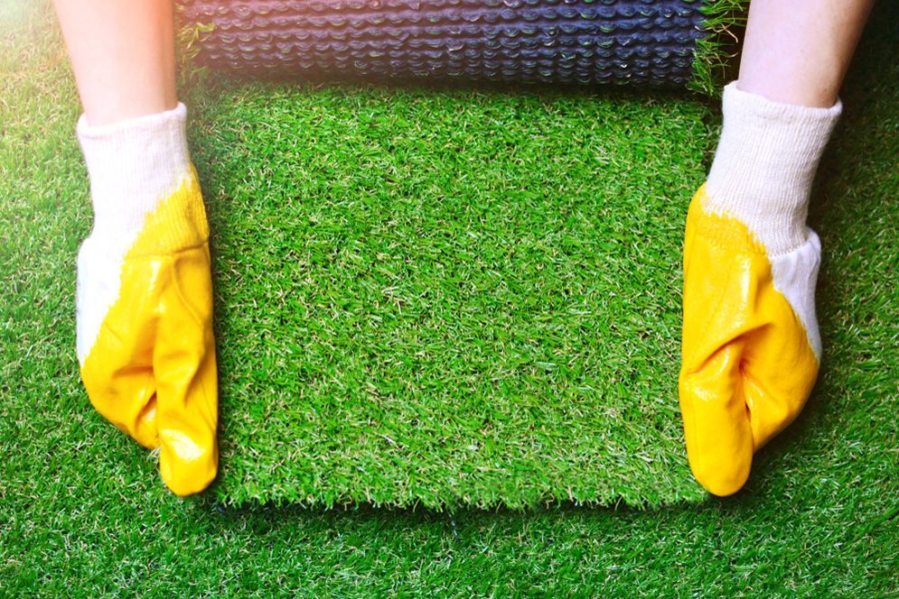 A Person Wearing Yellow Gloves is Holding a Roll of Fake Grass — Highfields Turf in Chinchilla,QLD