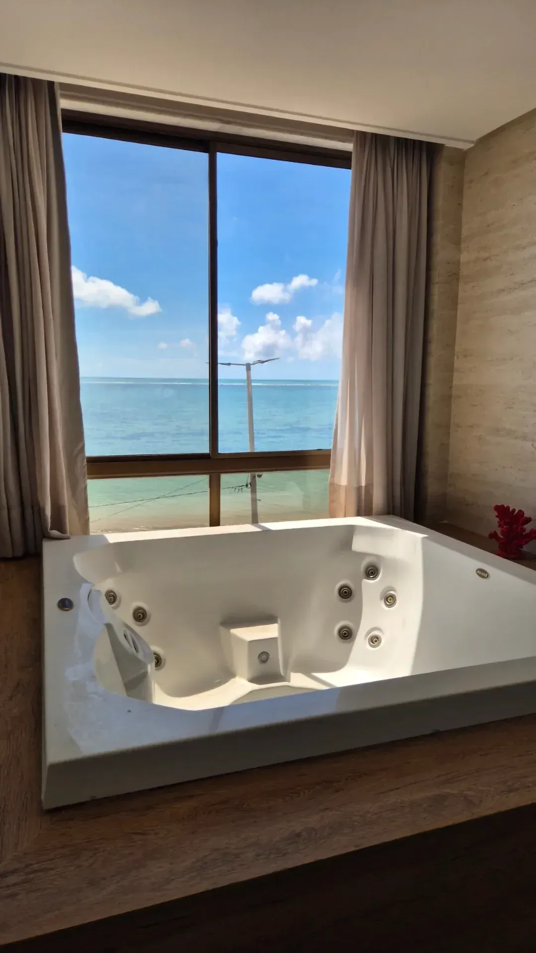 Banheira de hidromassagem de luxo ao lado de uma janela panorâmica com vista para um oceano azul.