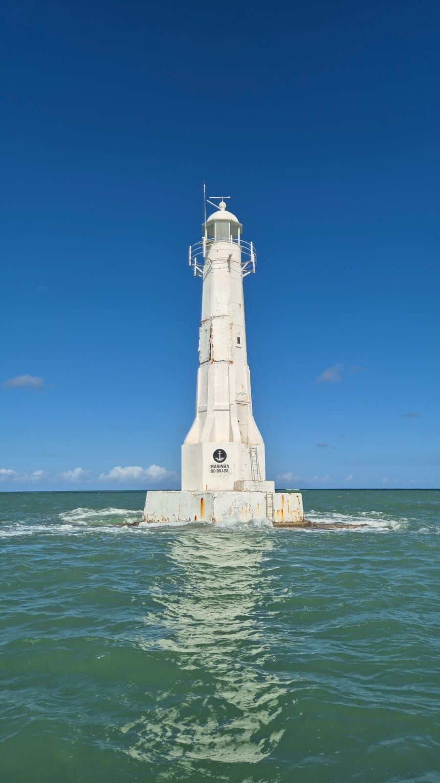 Farol branco em mar agitado azul-esverdeado sob um céu azul claro.
