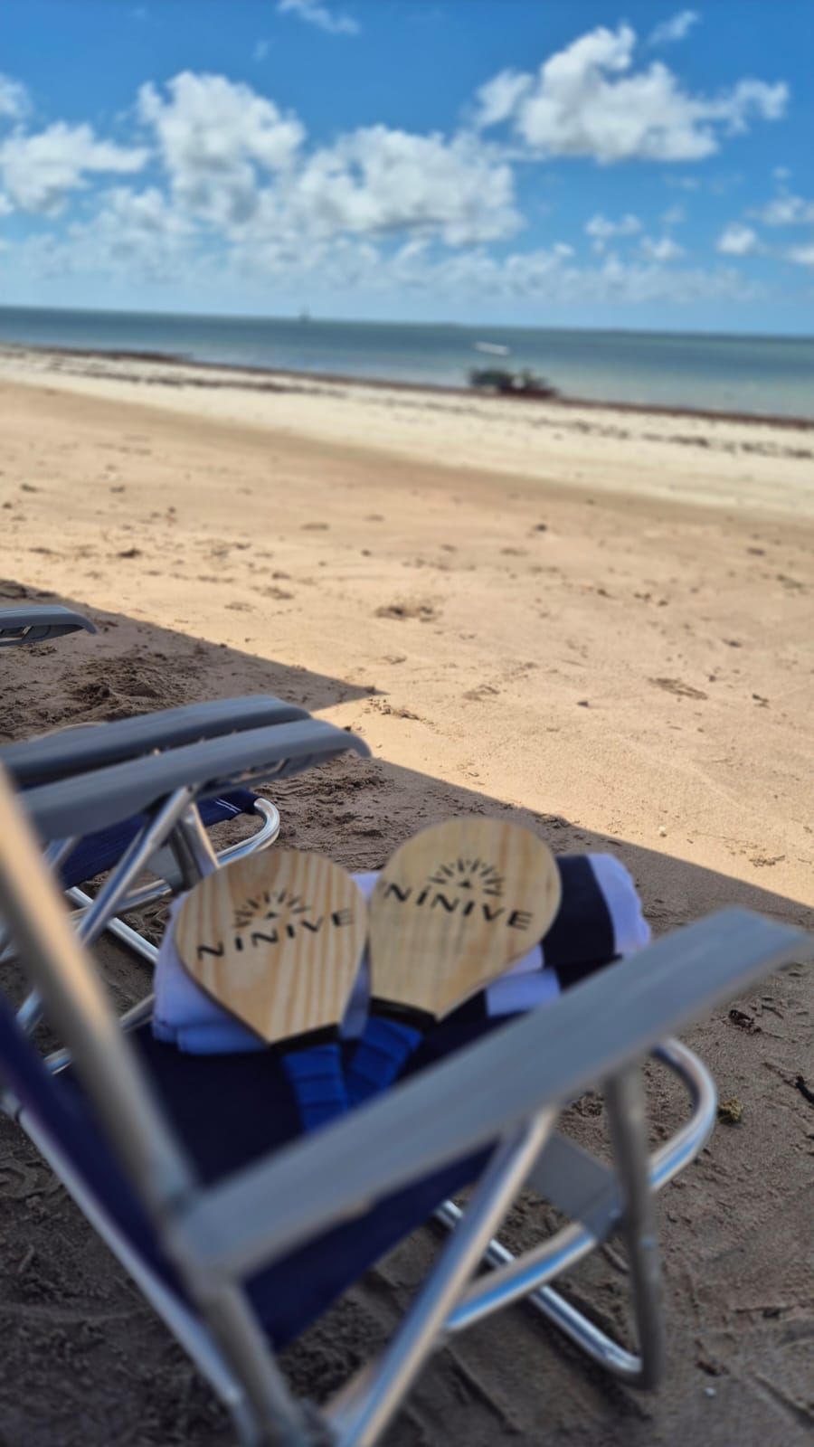Cadeira de praia com sandálias em uma faixa de areia sob um céu azul à beira-mar.
