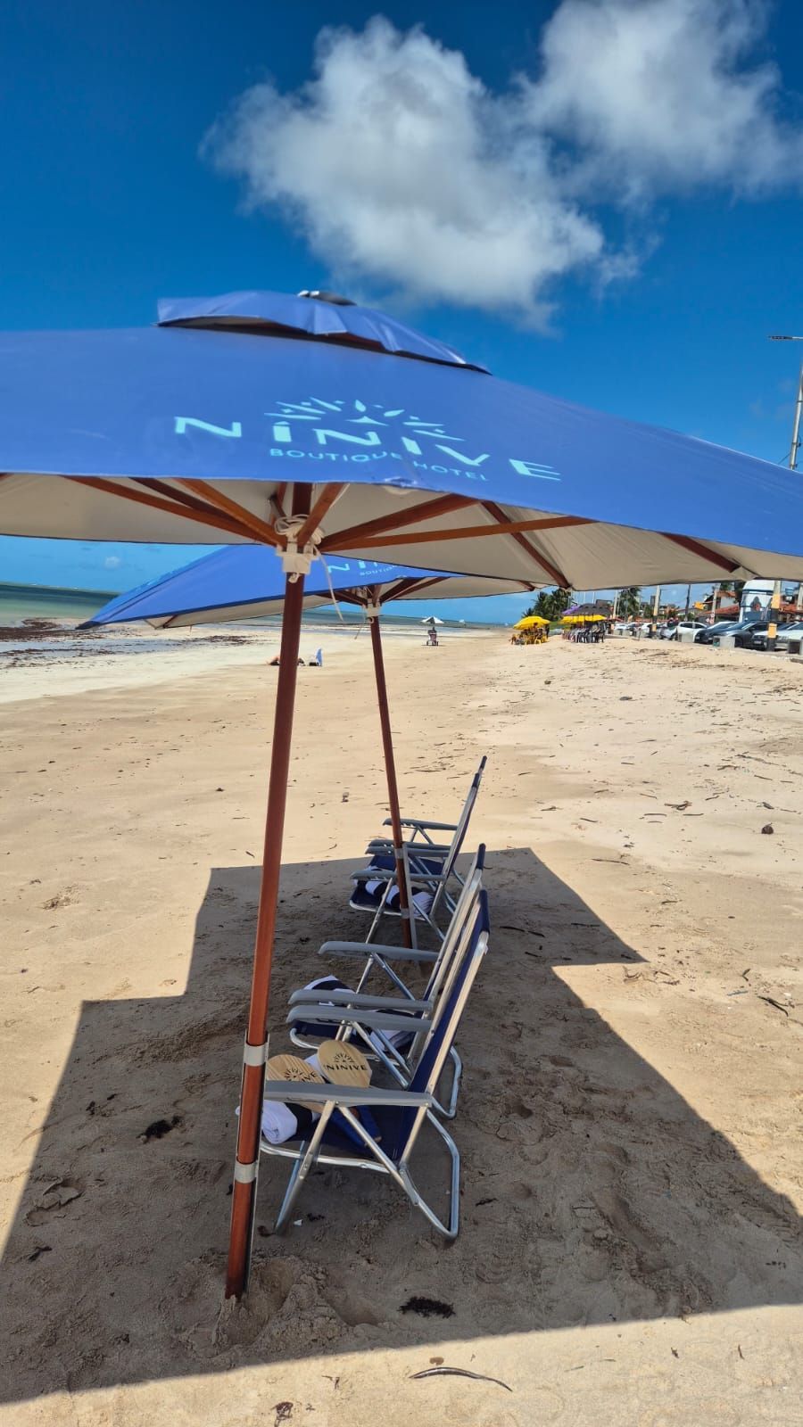 Um guarda-sol azul sombreando cadeiras de praia vazias em uma praia ensolarada de areia sob um céu azul.