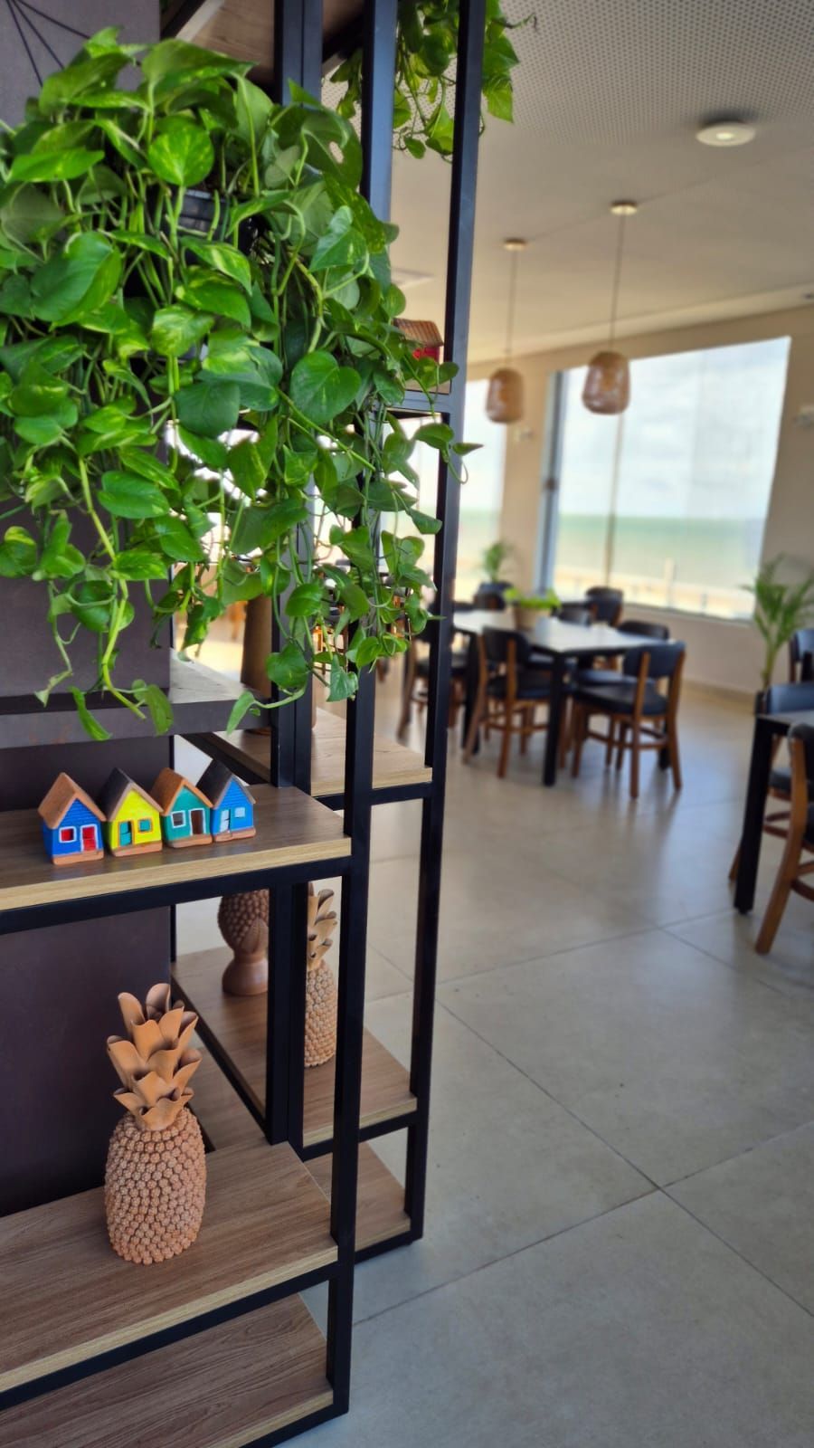 Prateleira preta com planta trepadeira verde, pequenos objetos decorativos coloridos em formato de casa.