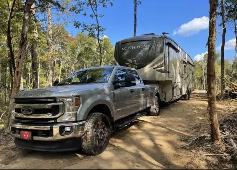 A truck is towing a rv down a dirt road.