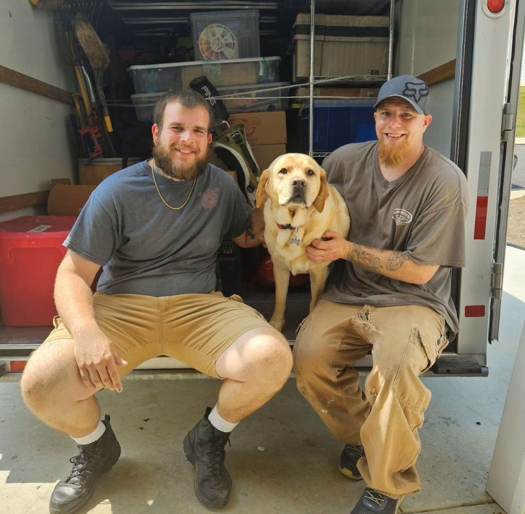 Two men are sitting in the back of a truck holding a dog