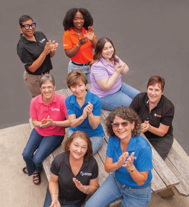 Group of people sitting and standing on wooden steps, smiling and clapping in a casual outdoor setting